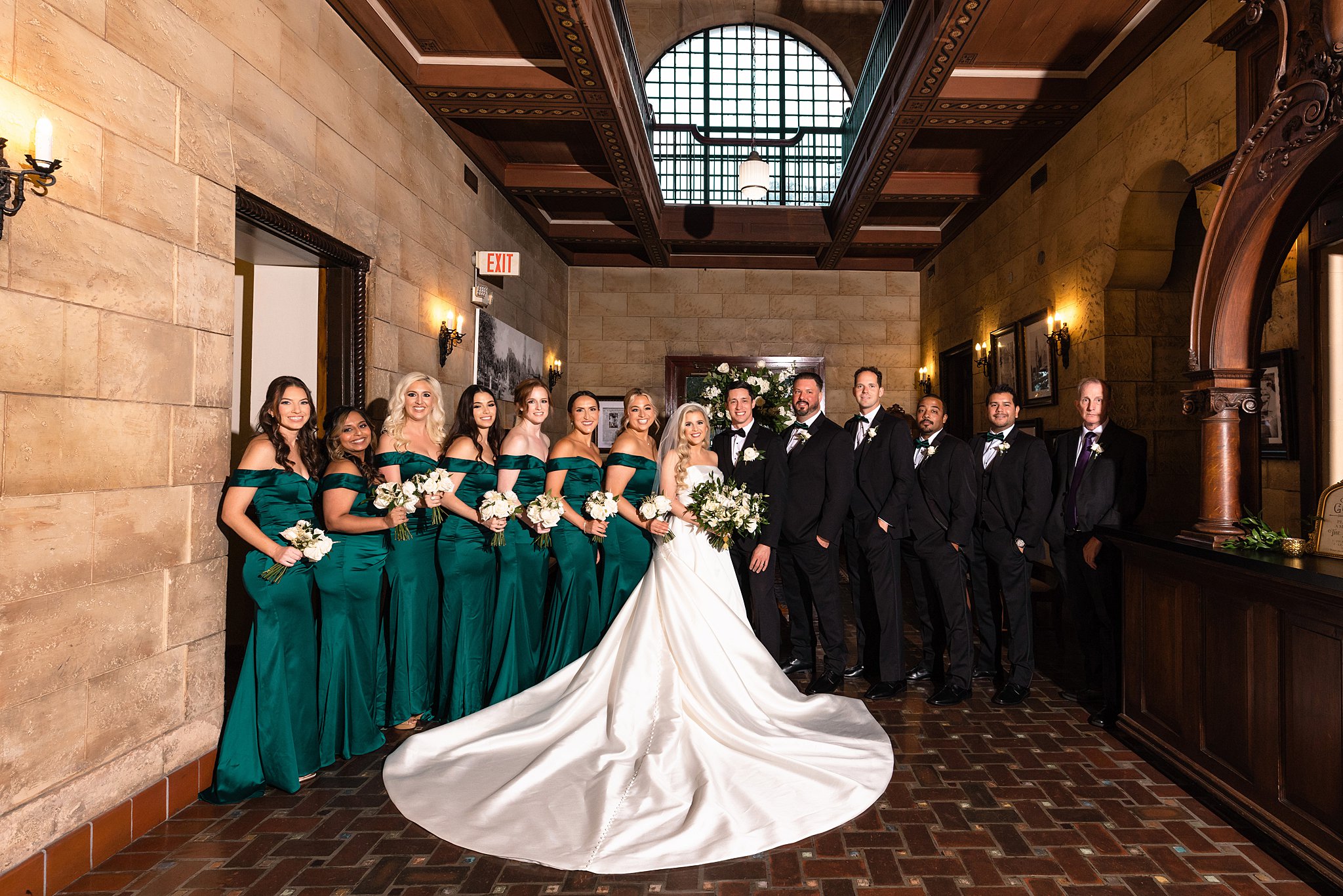 Newlyweds stand in the center of their large wedding party in an ornate lobby with the train fully laid out