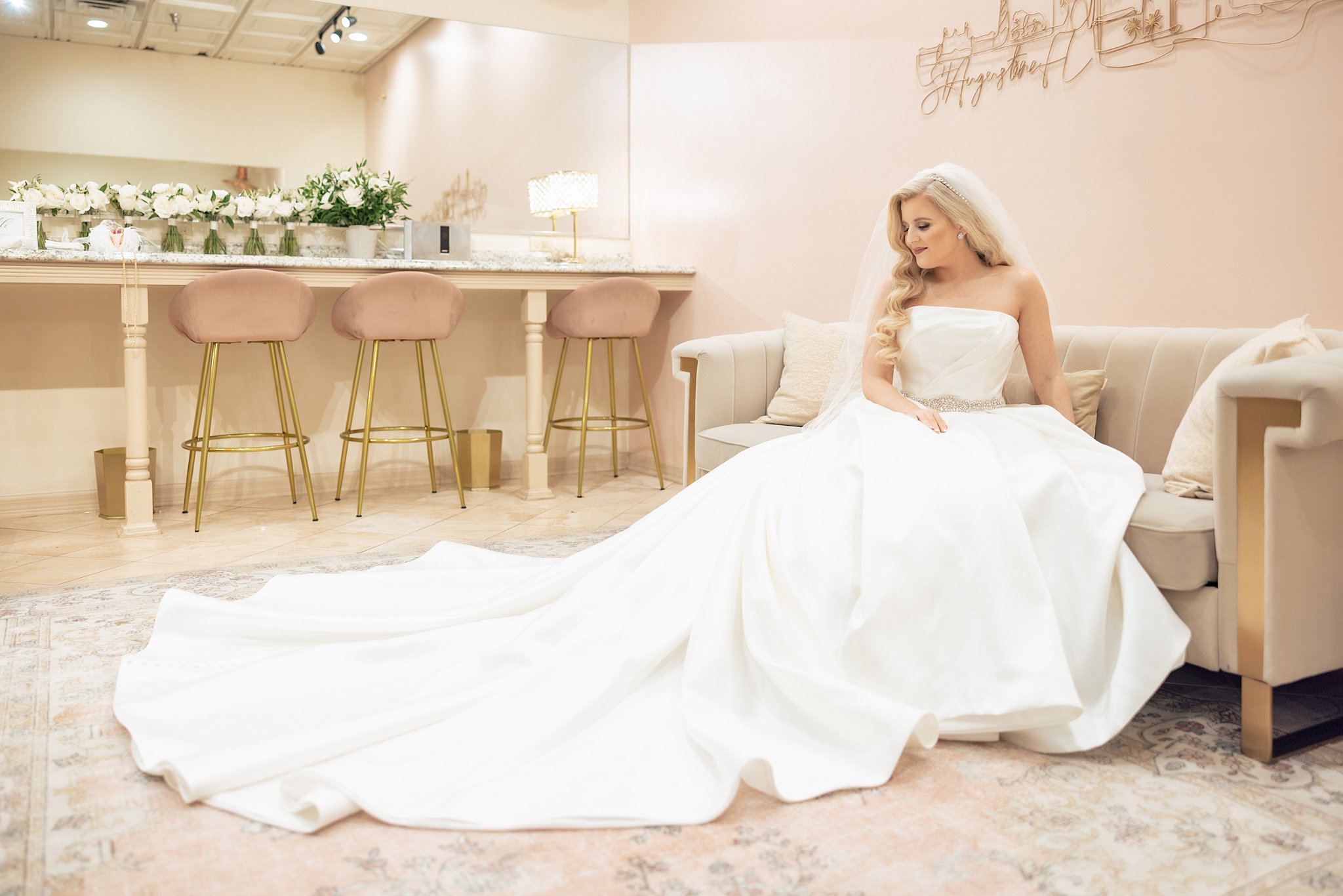 A bride sits on a couch in the getting ready room at the Treasury on the Plaza Wedding venue smiling down at her long train