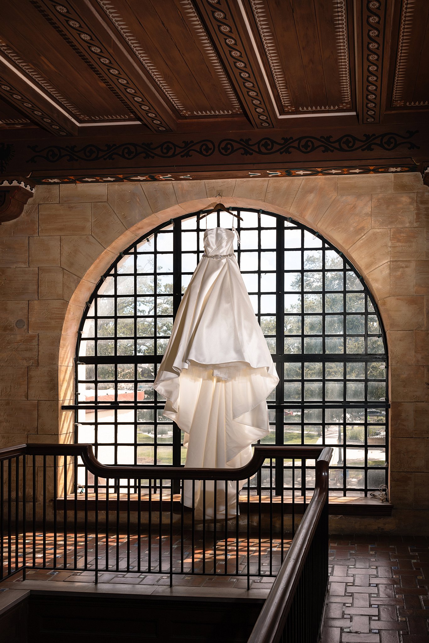 A silk wedding dress hands in the center of a large arched window at the Treasury on the Plaza Wedding venue
