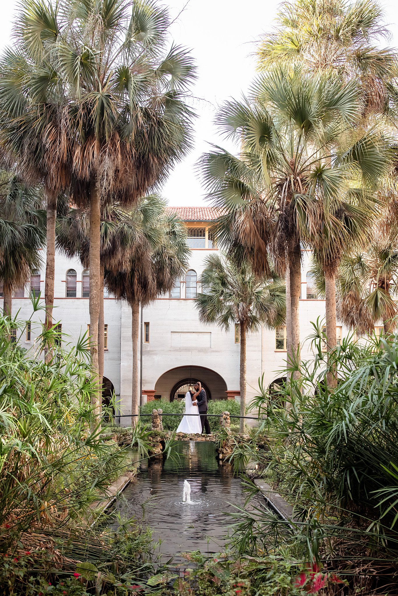 Newlyweds stand on a bridge in a garden at one of the st augustine wedding venues leaning in for a kiss