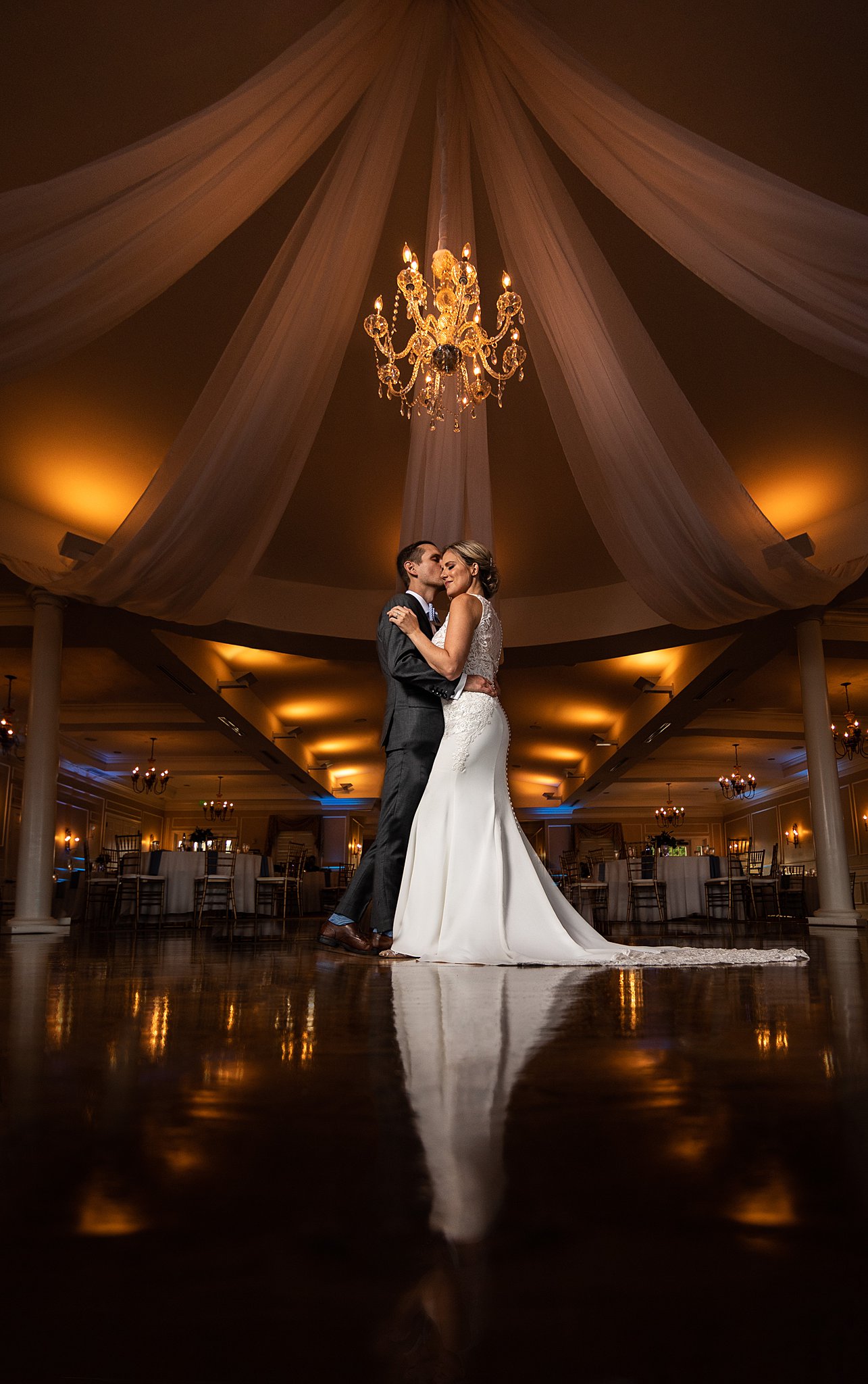 Newlyweds slow dance on an empty dance floor under a chandelier