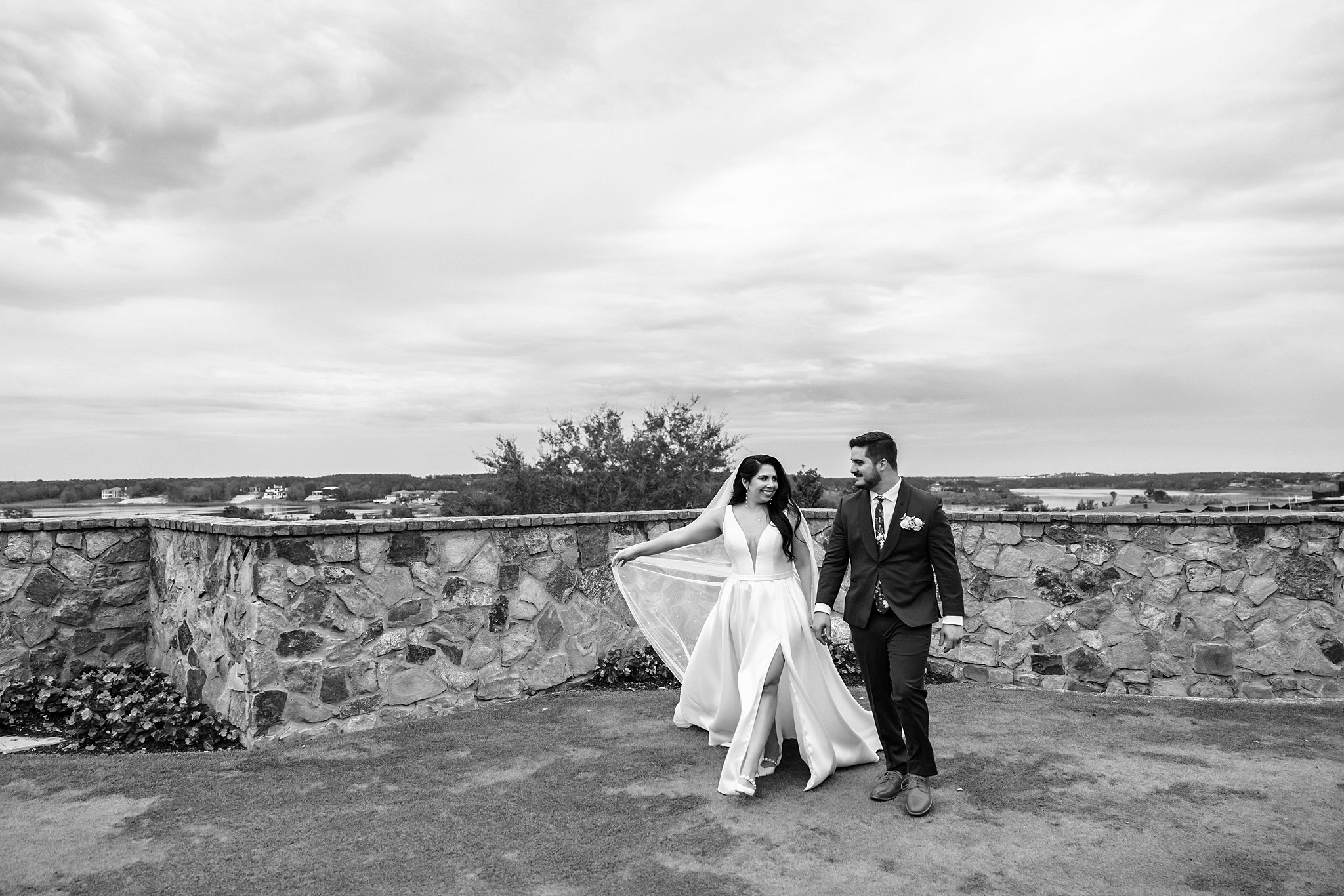 Newlyweds walk hand in hand on a garden terrace with stone walls
