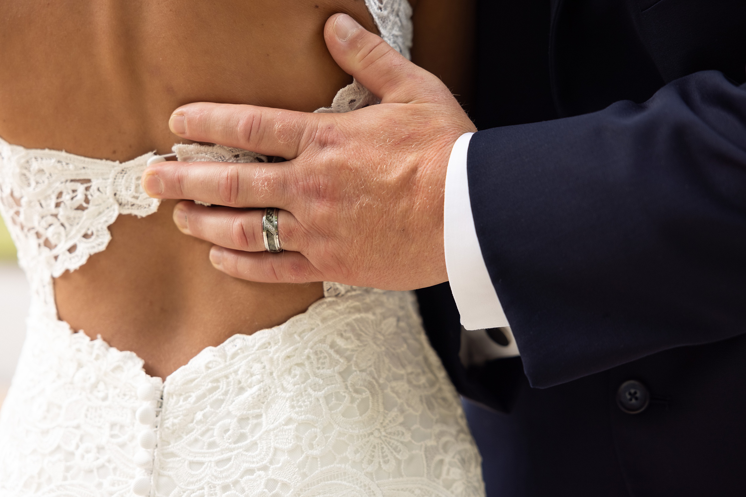 Details of a groom holding the back of his bride with a ring on and blue suit at their Casa de solana wedding