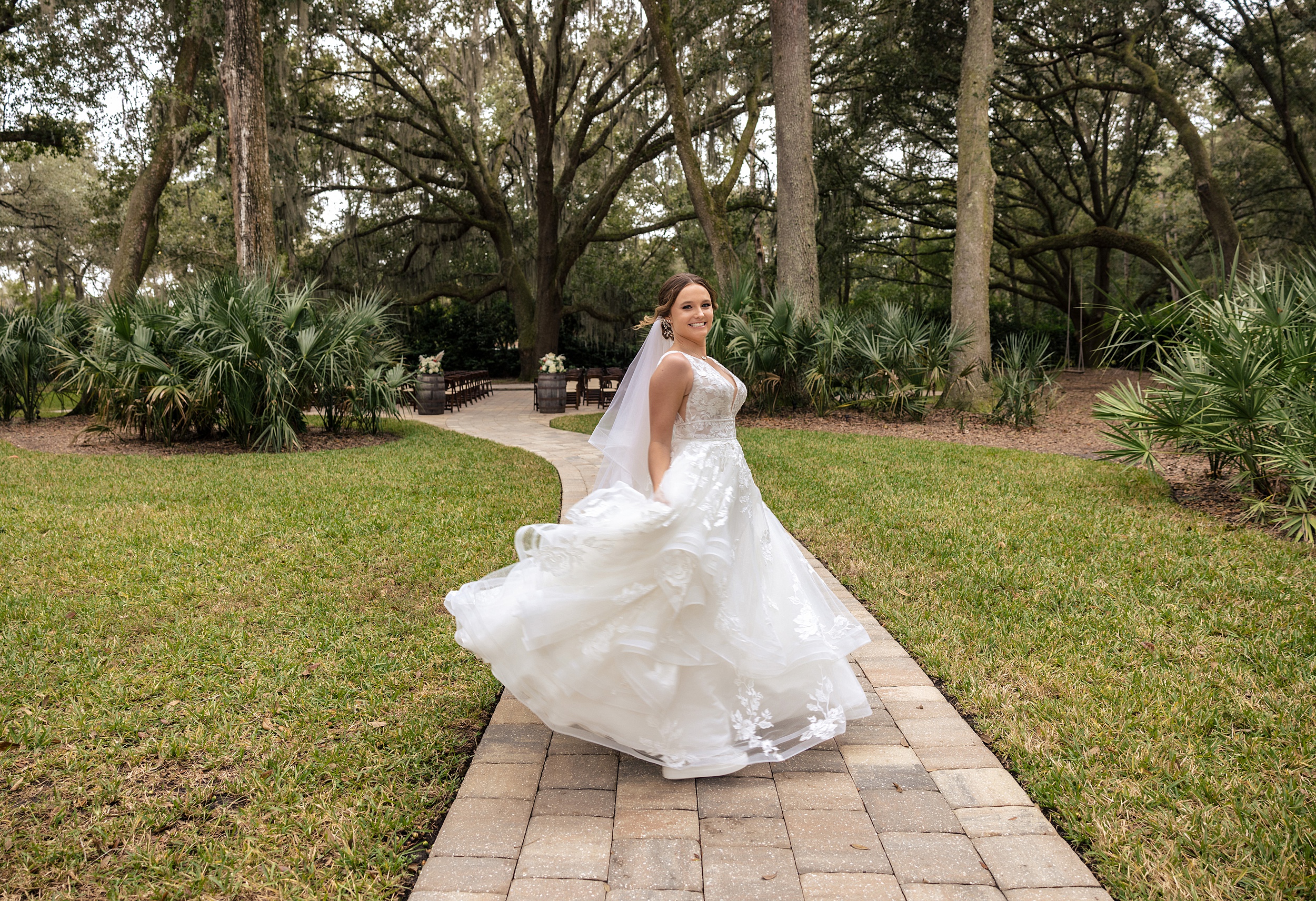 A bride twirls in her dress on a patio walkway under oak trees