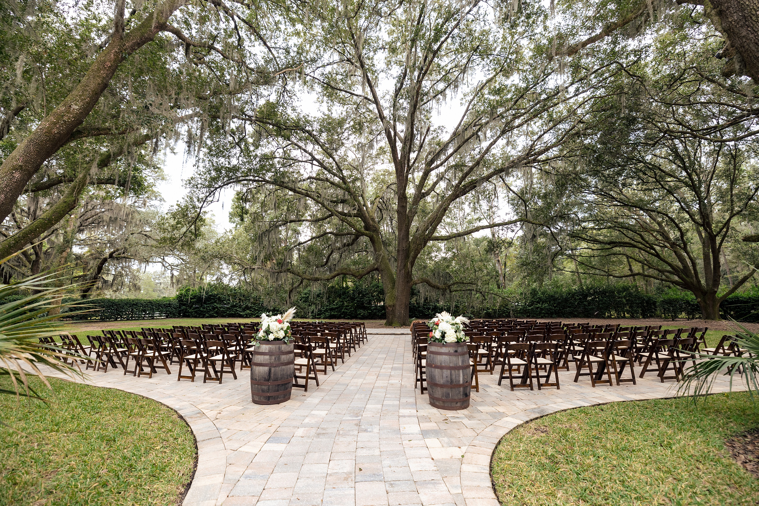 Details of a bowing oaks wedding ceremony set up with wooden chairs on a patio under large oak trees