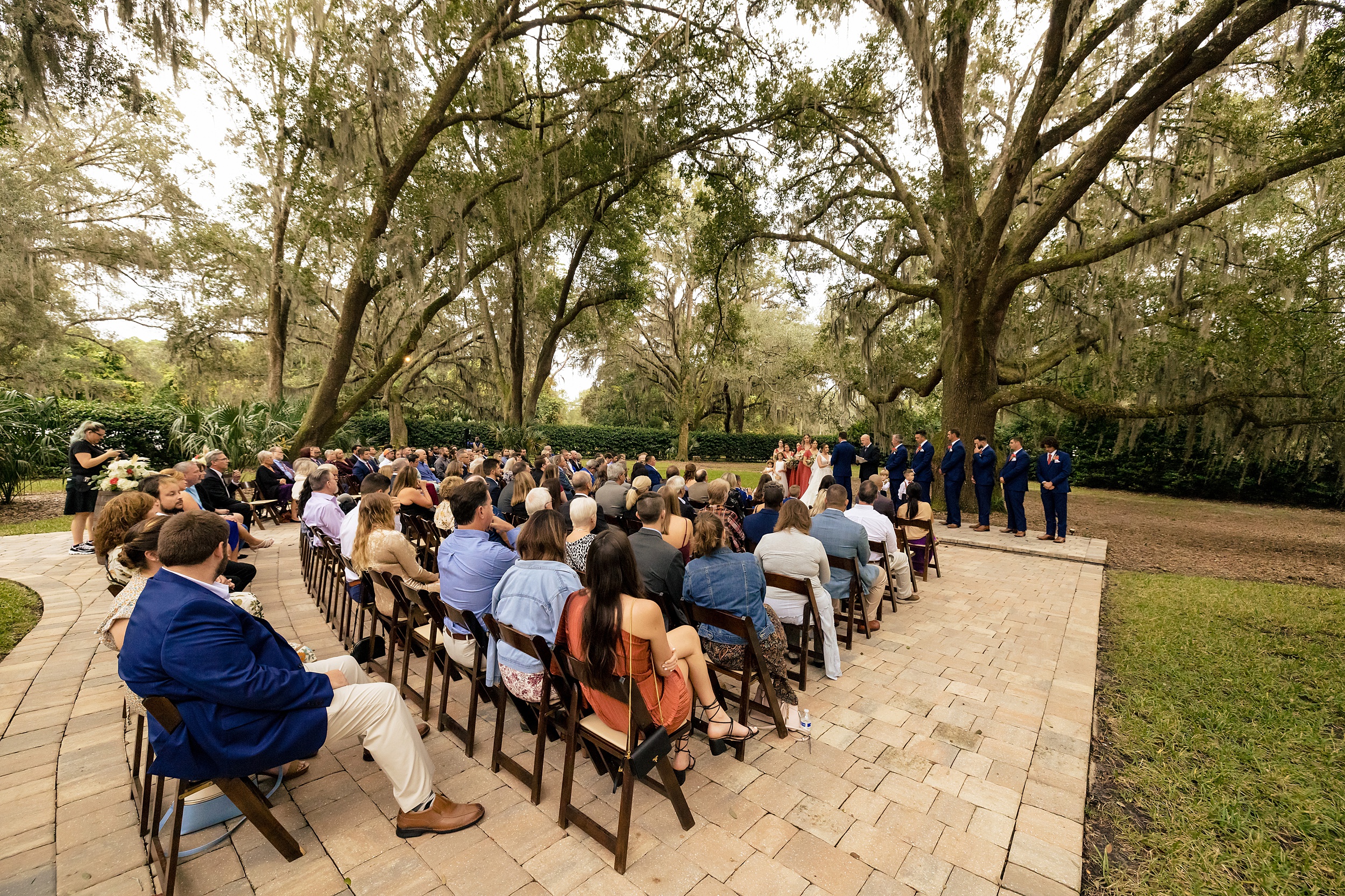 A view of a bowing oaks wedding ceremony on an outdoor patio under a canopy of large oak trees
