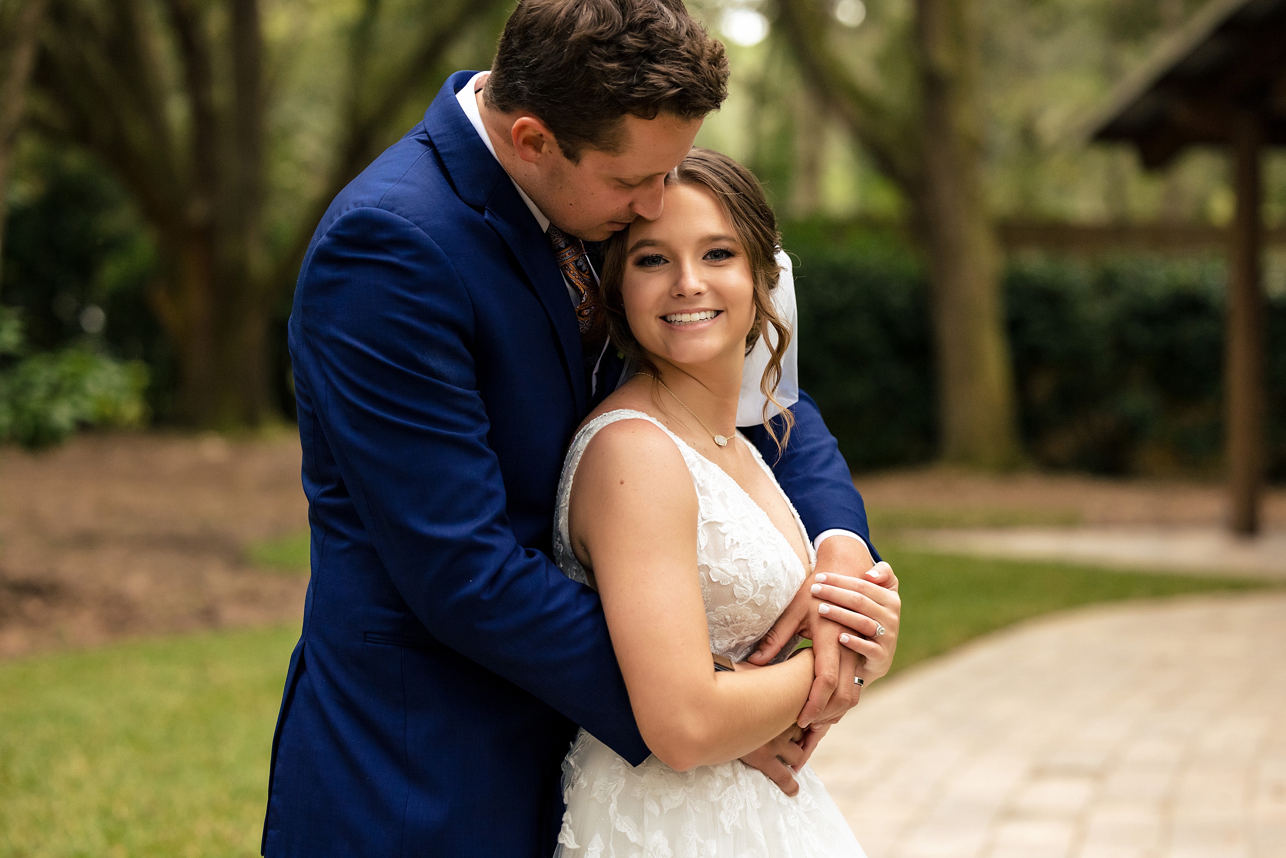 Newlyweds embrace while standing on a patio in a garden in a blue suit and lace dress
