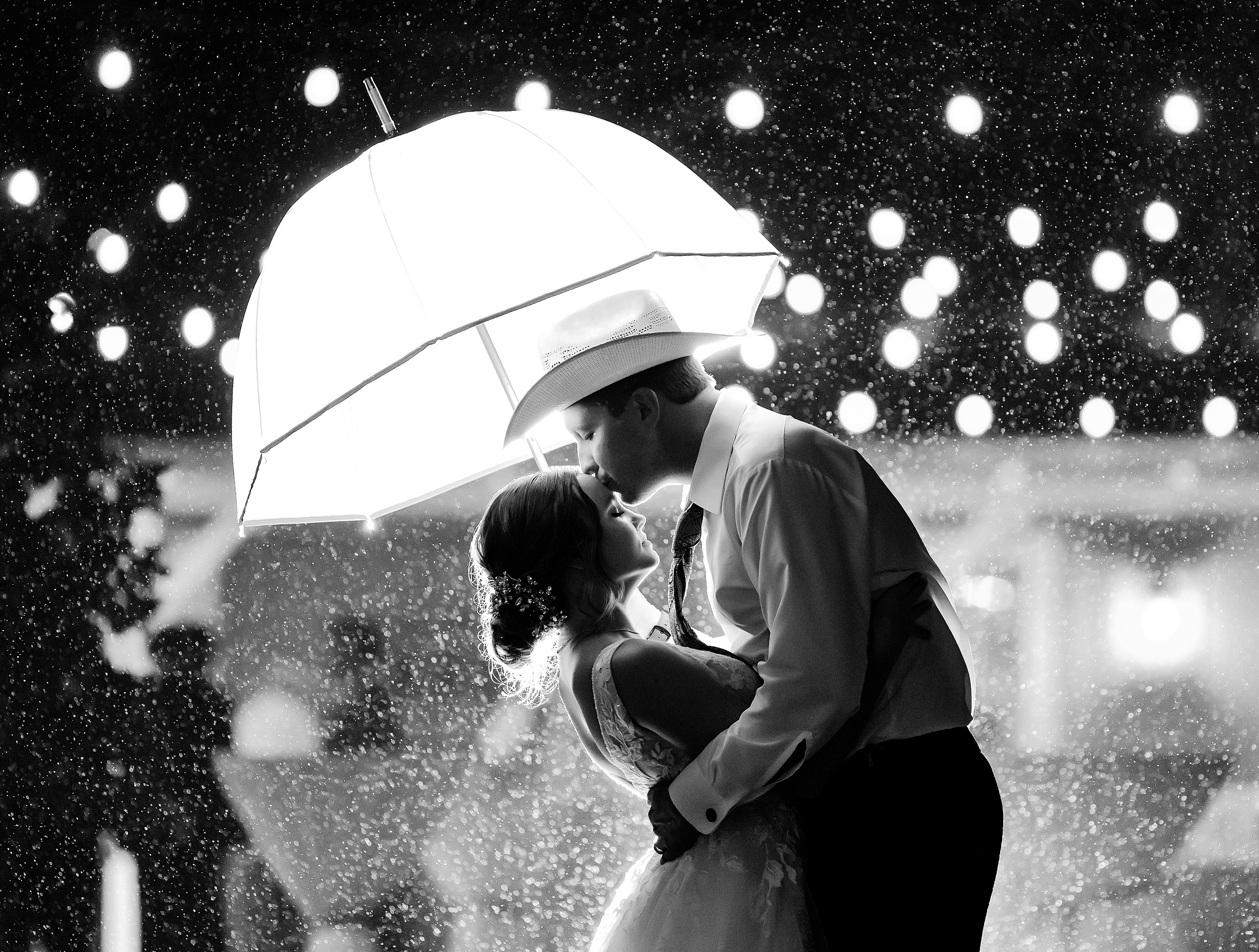 A groom kisses the forehead of his bride under an umbrella in the rain at their bowing oaks wedding