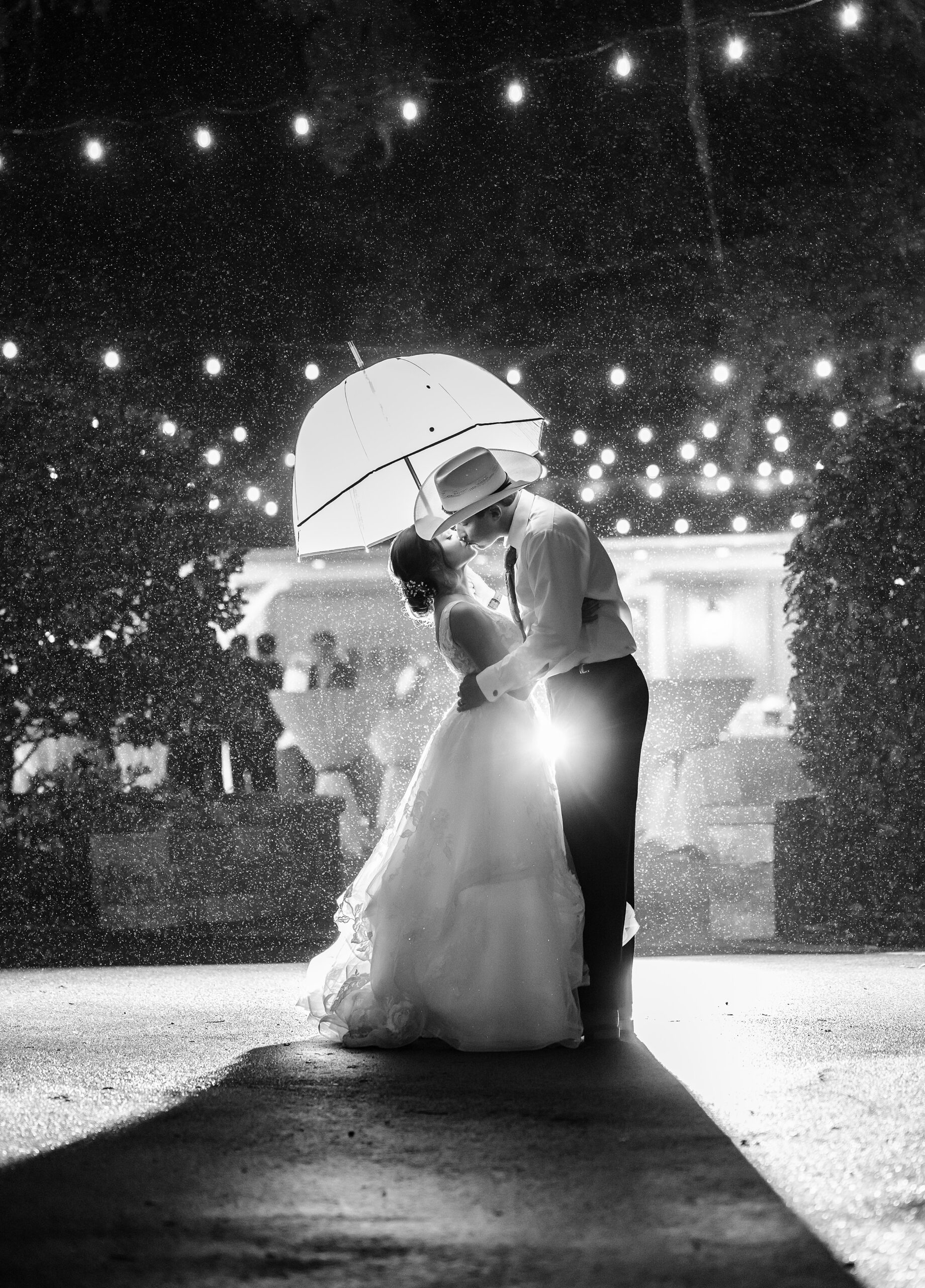 Newlyweds kiss under an umbrella in the rain on the patio of their bowing oaks wedding