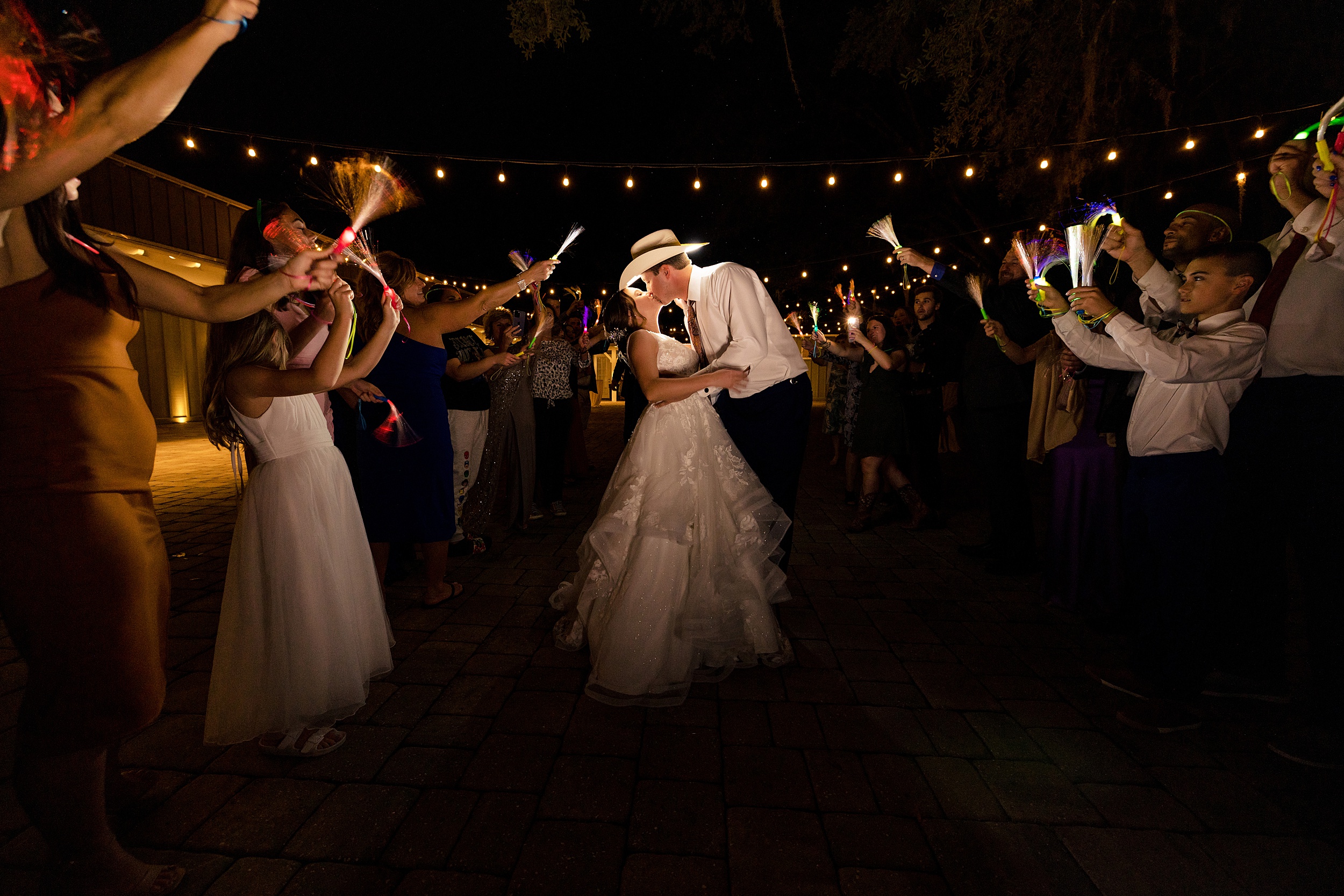 Newlyweds kiss while exiting their bowing oaks wedding reception with guests surrounding them with glow wands