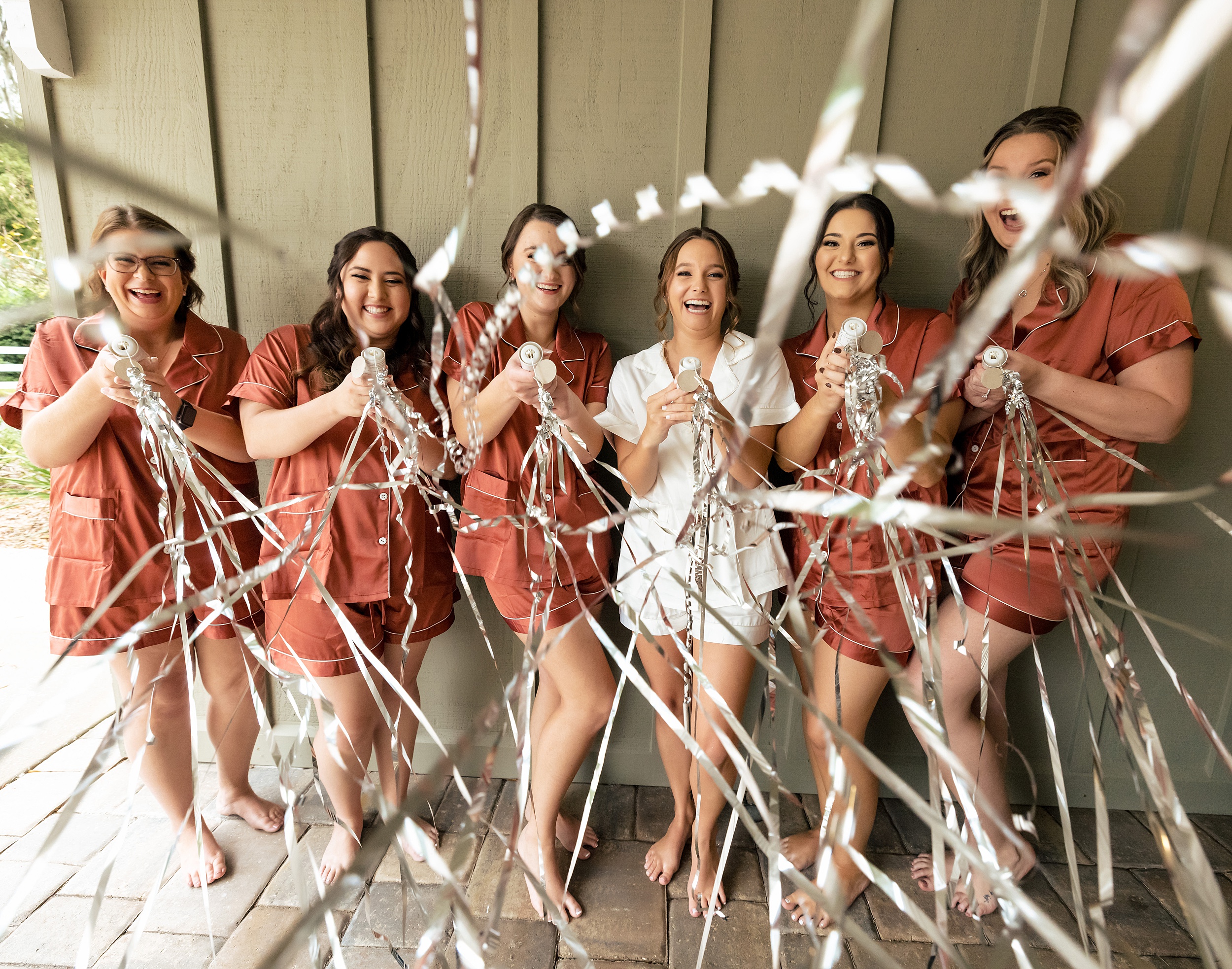 A bride shoots streams while laughing with her bridal party on a patio