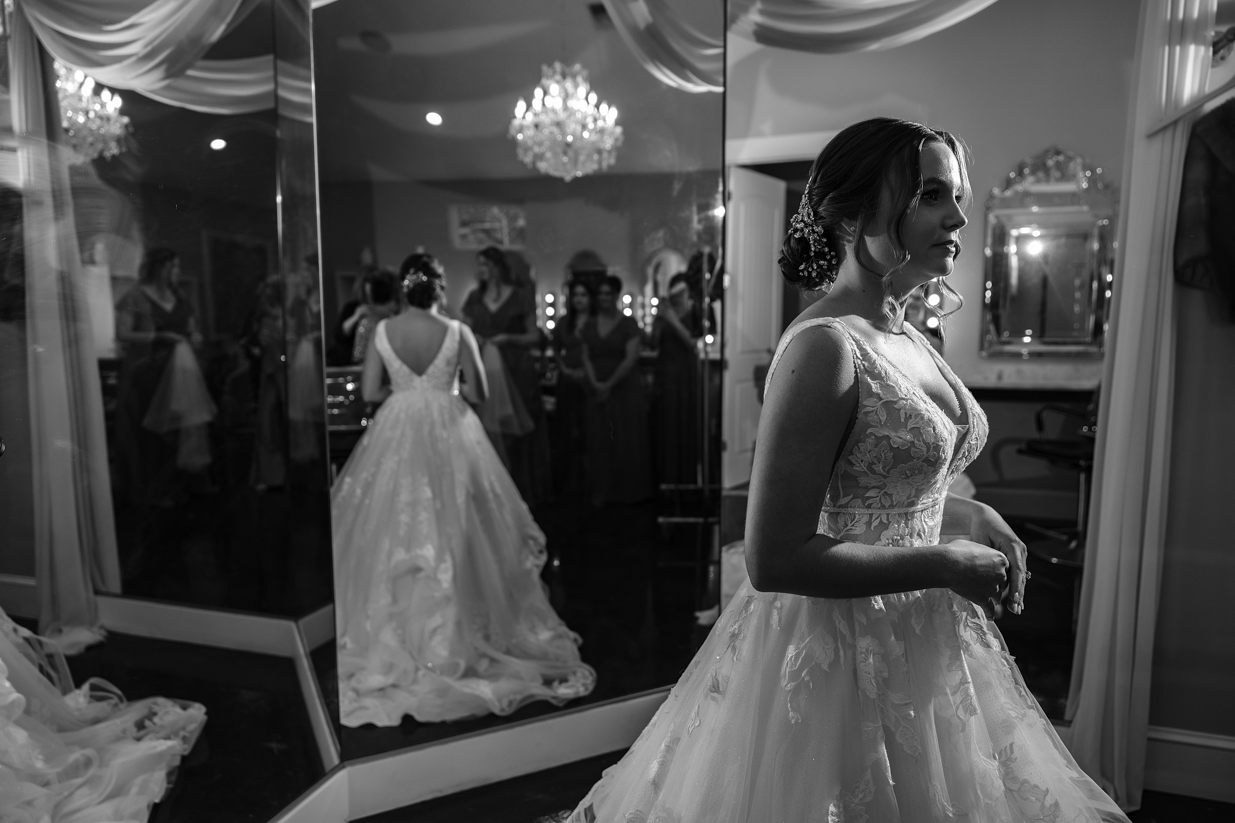 A bride stands in a large mirror while getting ready with her party