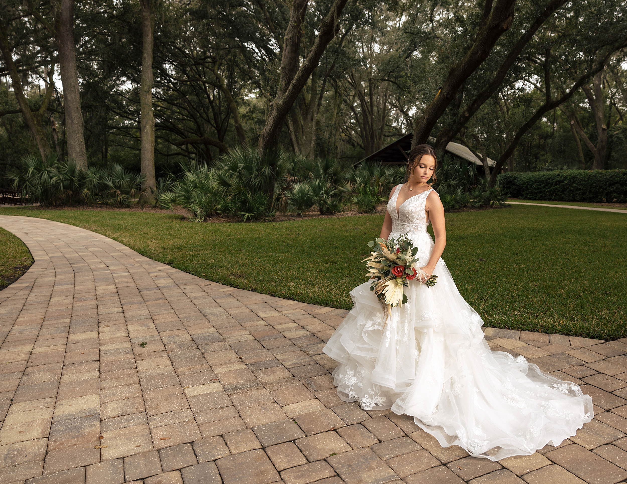 A bride glances down her shoulder while walking down a bowing oaks wedding venue patio path
