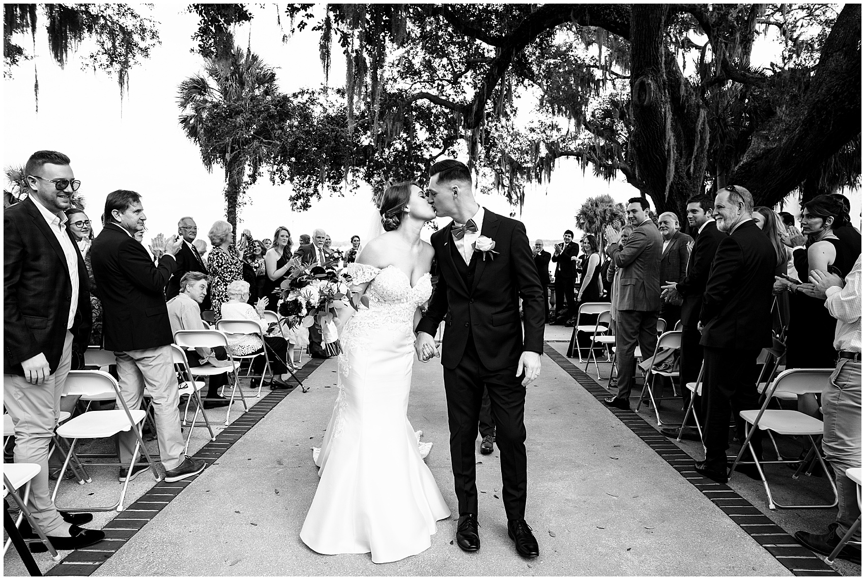 Newlyweds kiss in the aisle under a large oak tree to end their club continental wedding ceremony