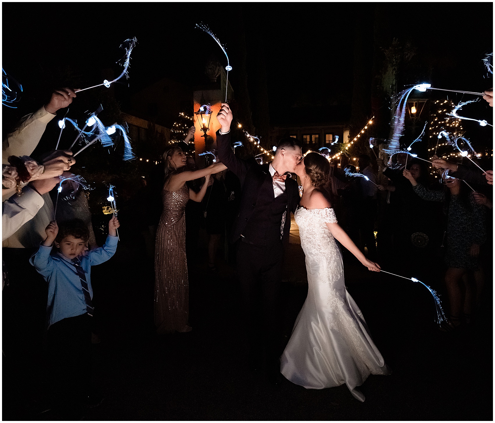 Newlyweds kiss under an aisle of sparkler sticks being waved by guests at the end of their club continental wedding