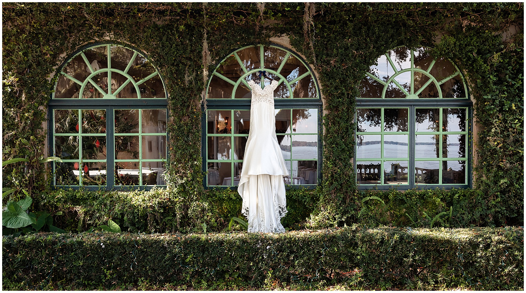 A wedding dress hangs from a large arched window on a wall covered in vines at the club continental wedding venue