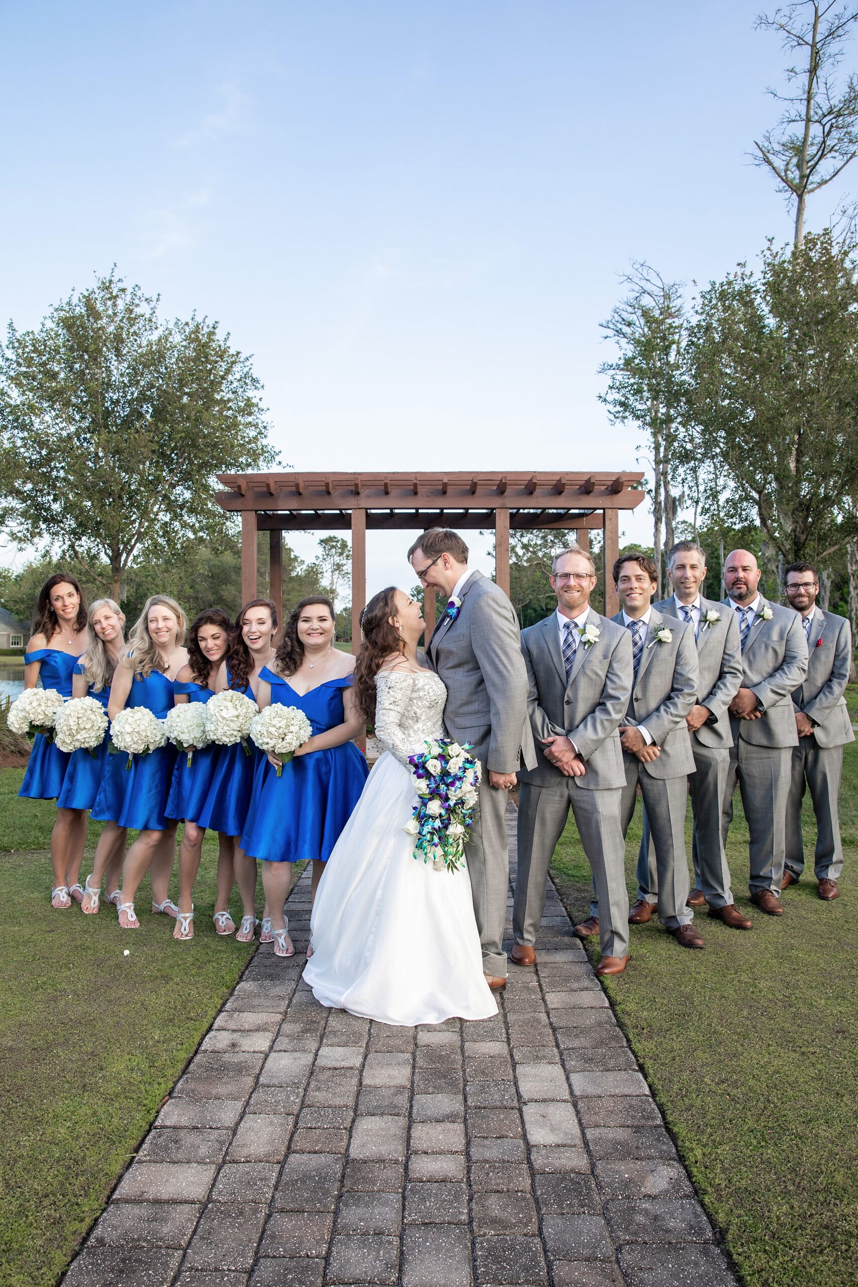Newlyweds stand nose to nose while their wedding party stands on either side of them in front of a pergola at their deercreek country club wedding