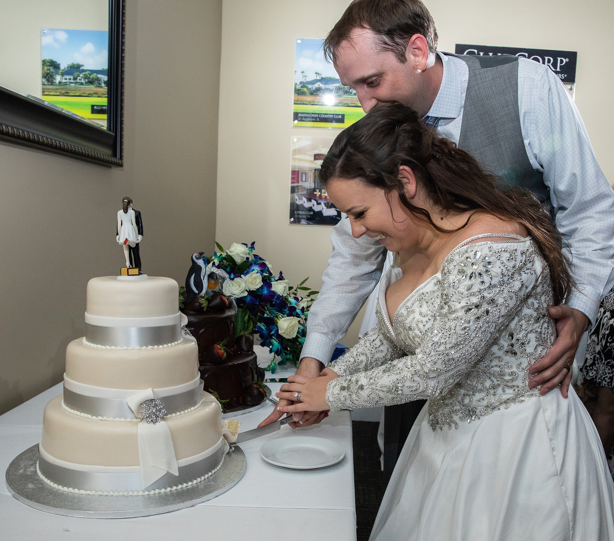 Newlyweds cut their three tier cake together in a grey vest and embroidered dress