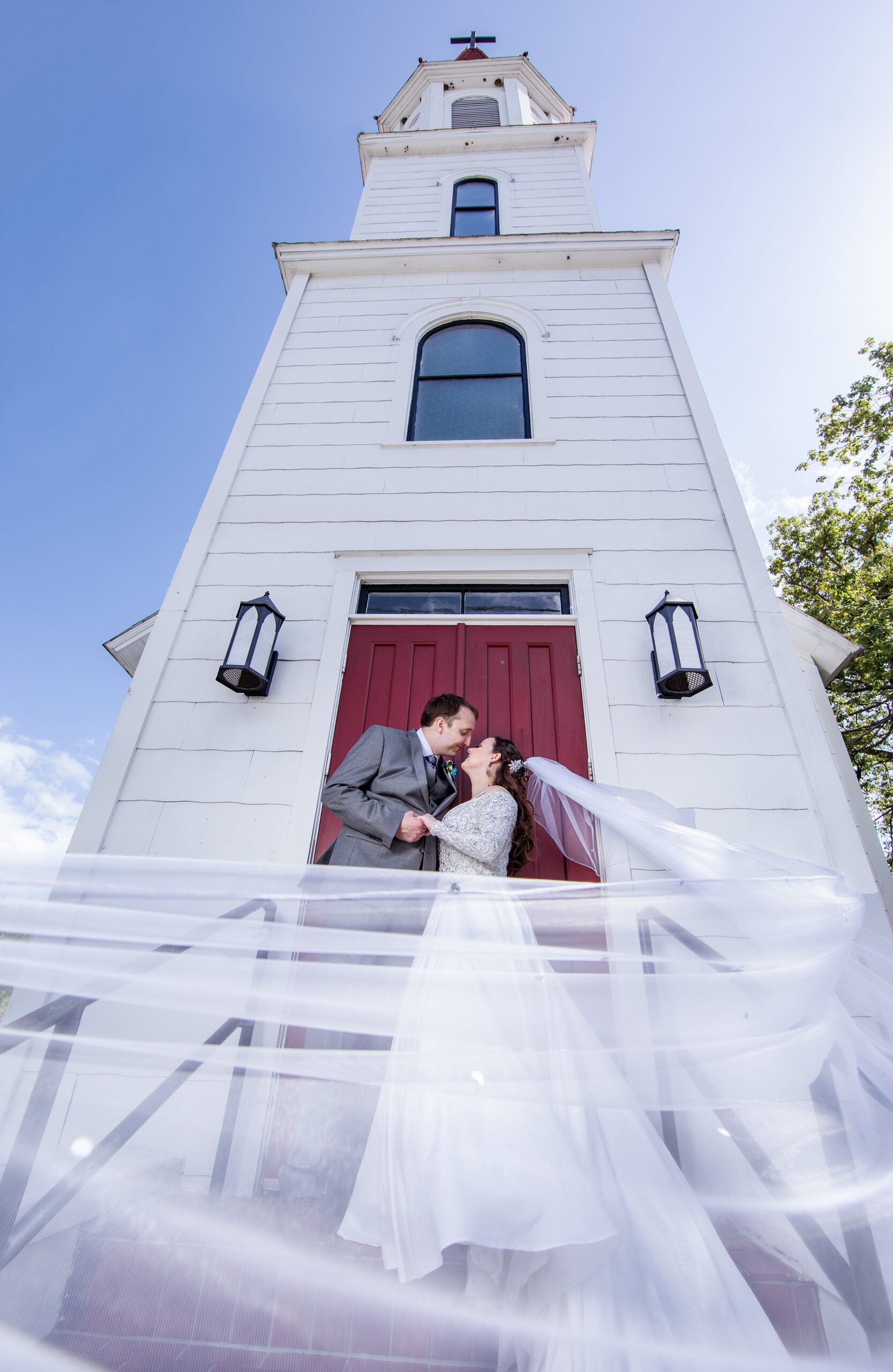 Newlyweds lean in for a kiss while standing on the steps of an old chapel with the veil flowing around them at their deercreek country club wedding