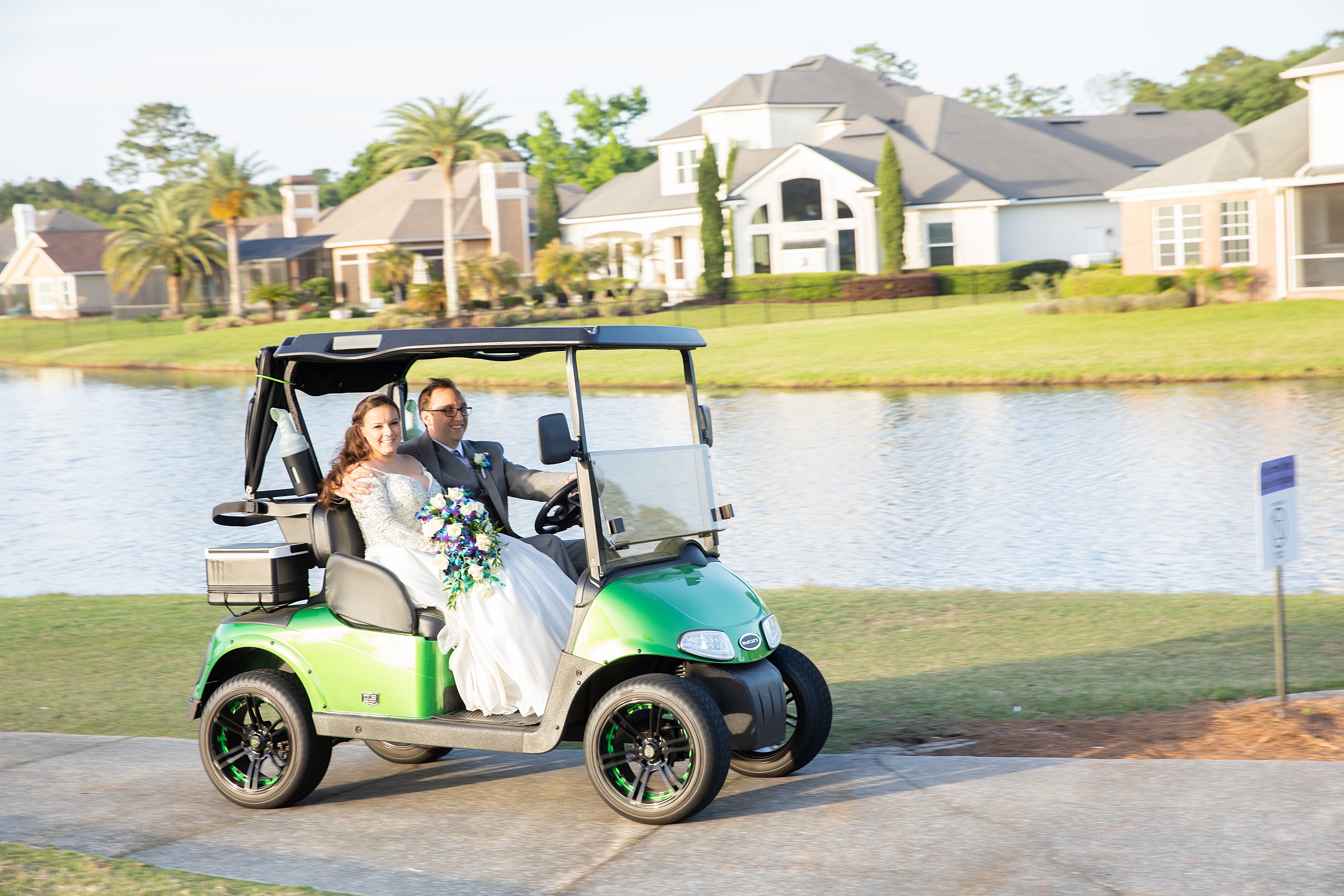 Newlyweds ride a golfcart down a path along a lake