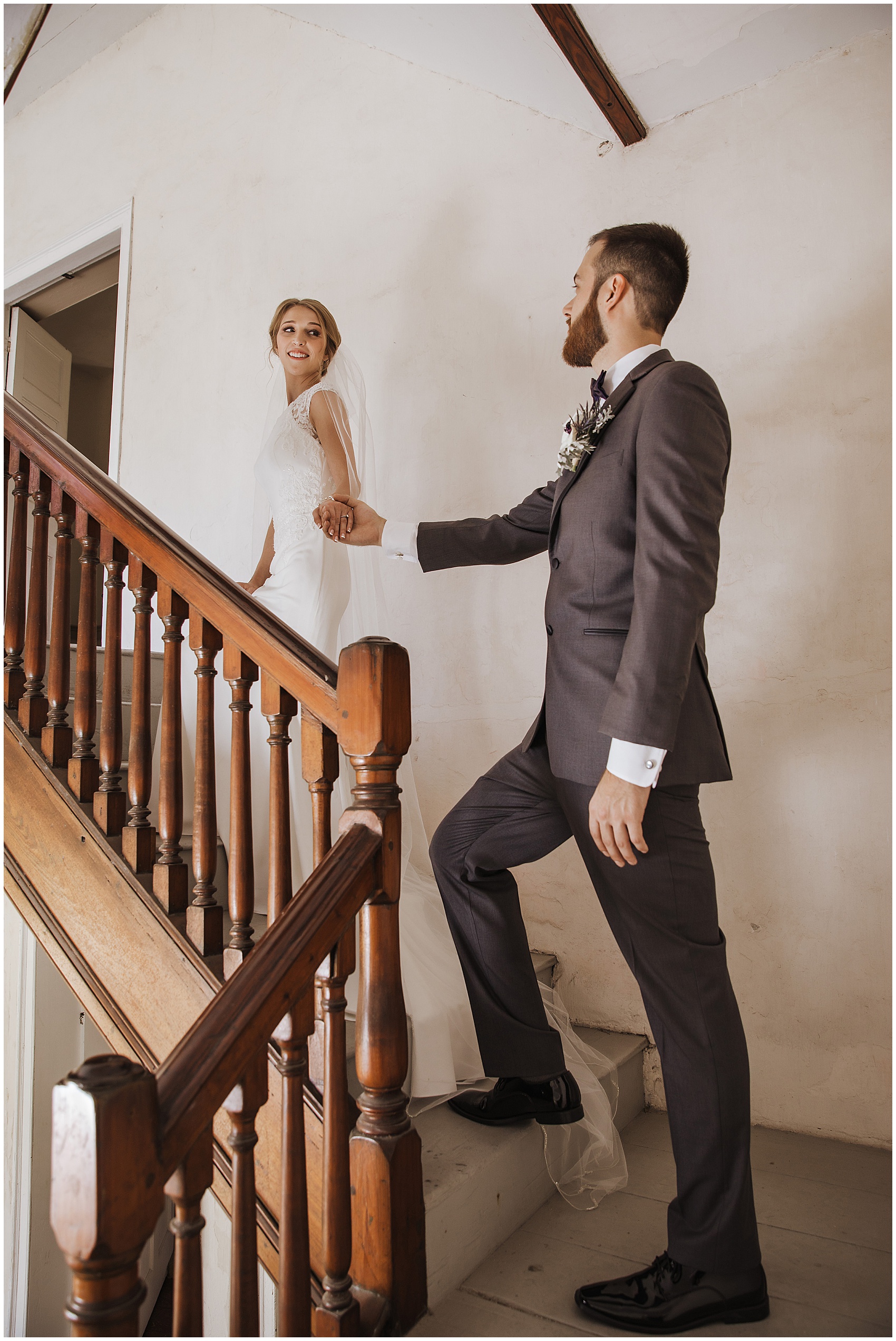 A bride leads her groom up a set of stairs by the hand
