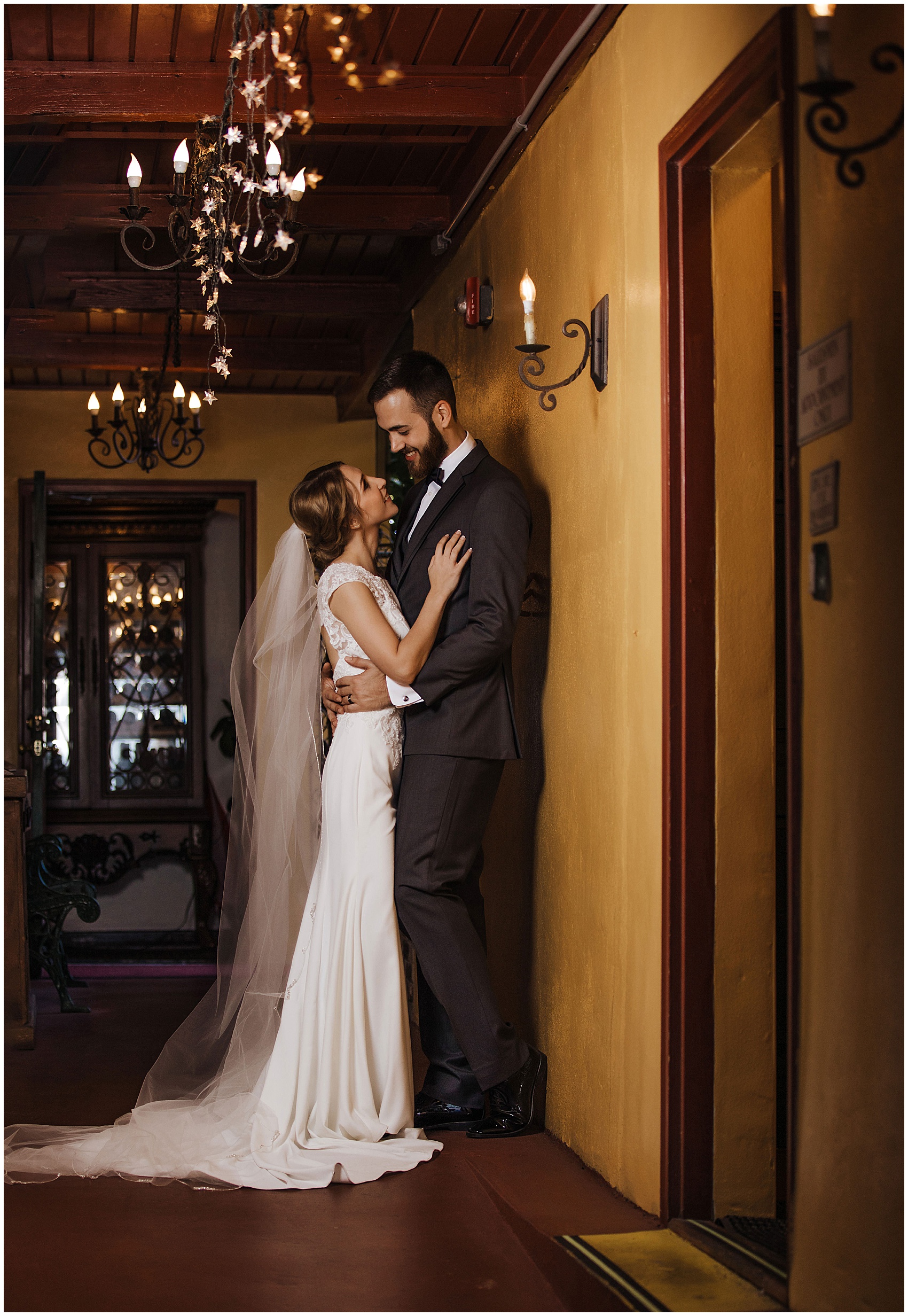 Newlyweds lean against a wall smiling at each other in a hallway at their flagler college wedding