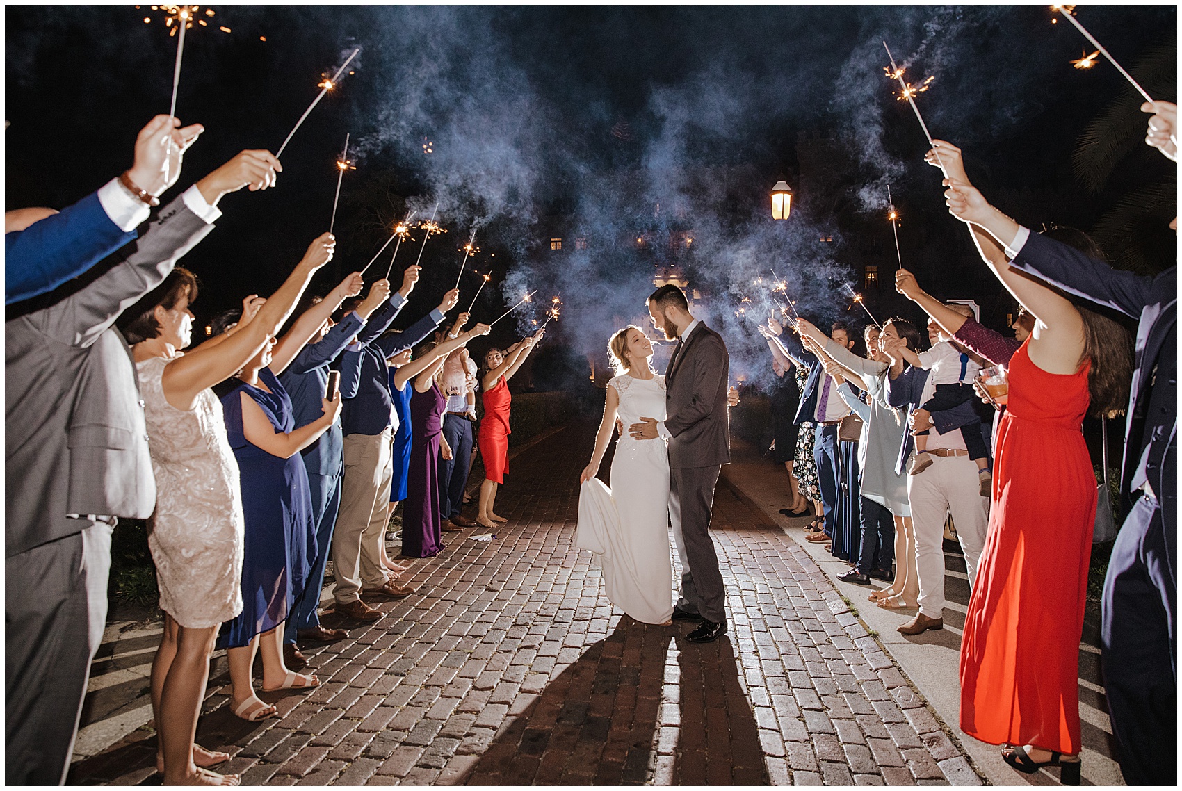 Newlyweds embrace in the middle of an aisle of guests holding sparklers at the end of their flagler college wedding