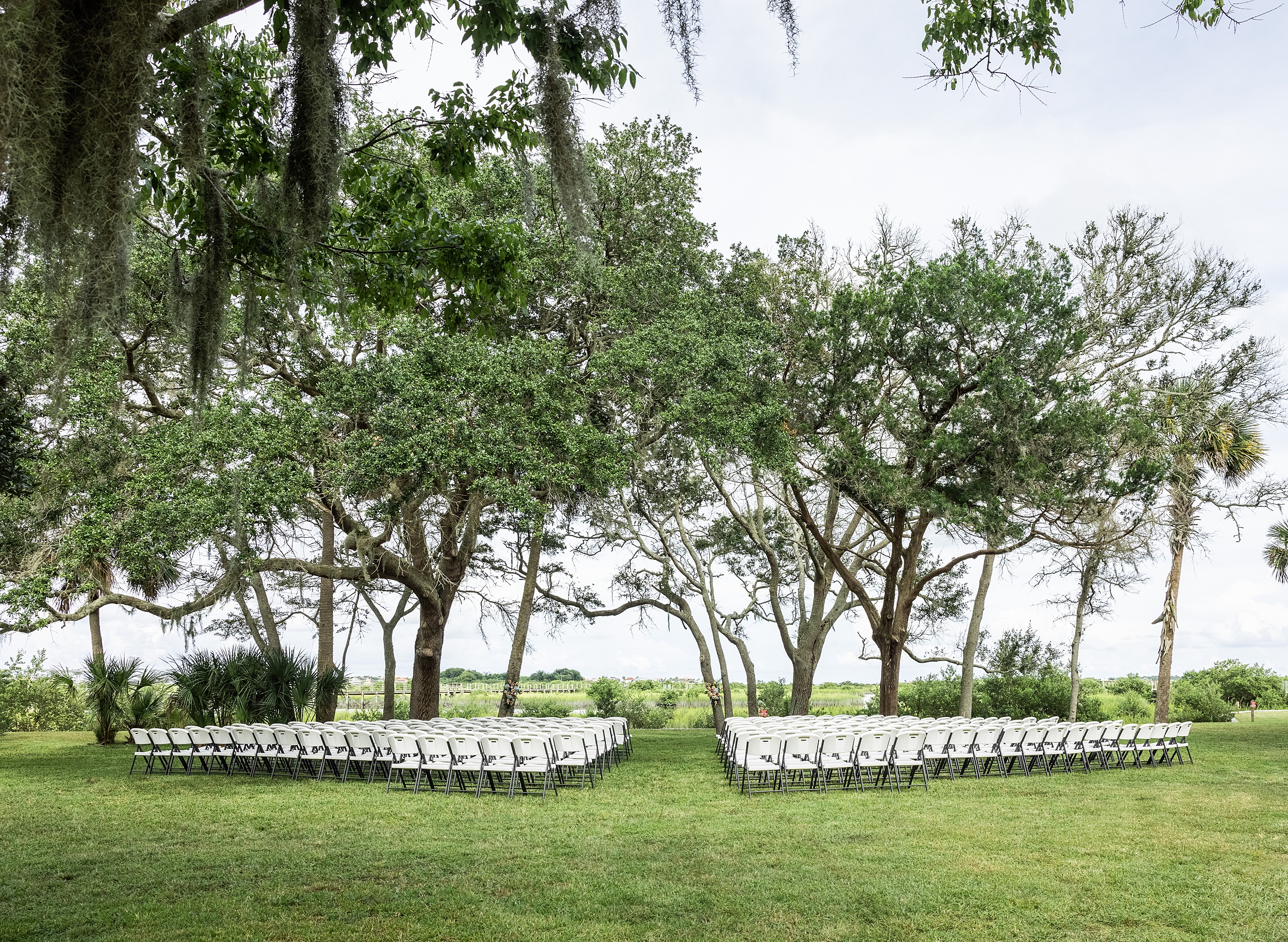 Details of a fountain of youth wedding ceremony set up on a grassy lawn under oak trees with white chairs