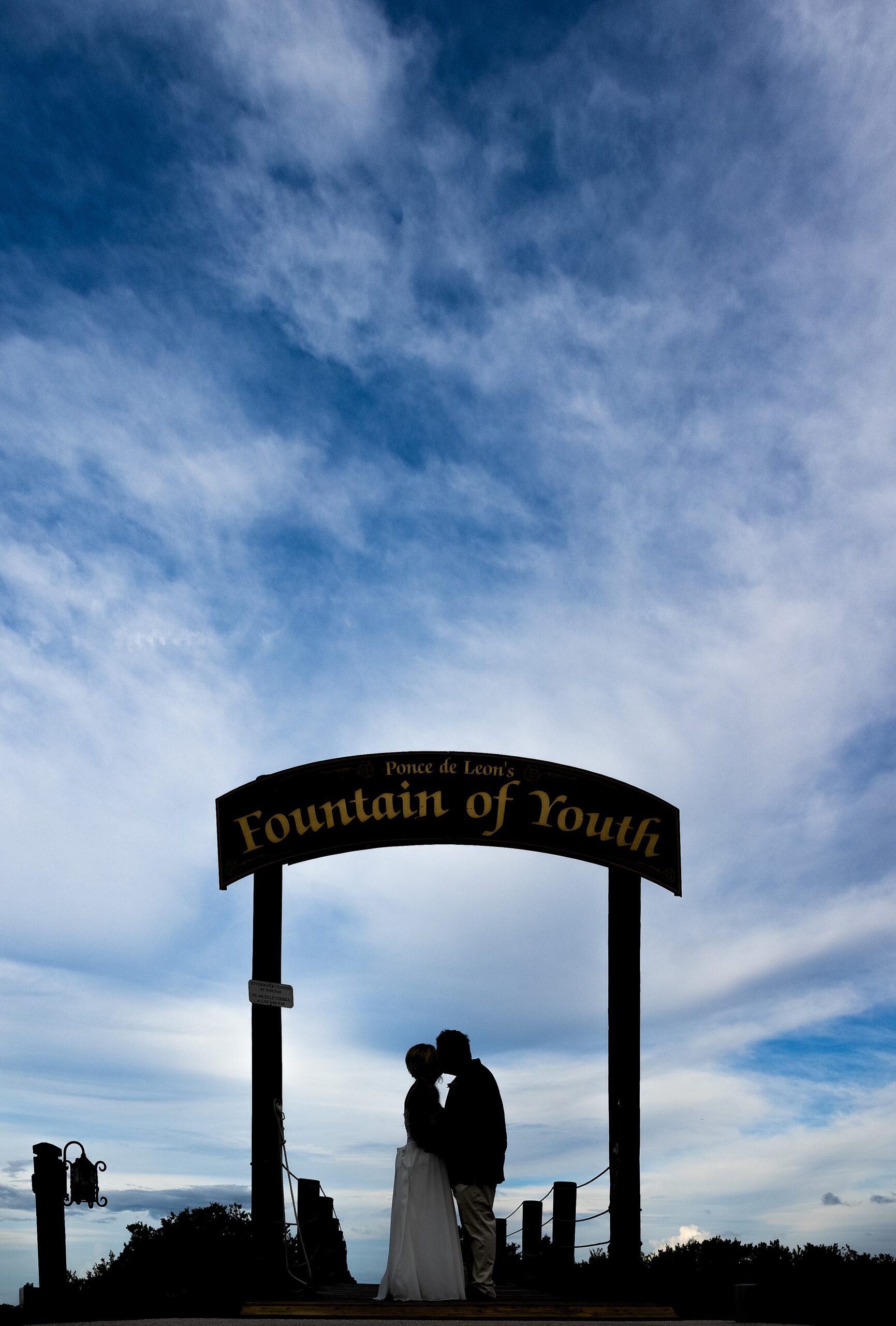 Newlyweds kiss in silhouette under the sign at their fountain of youth wedding