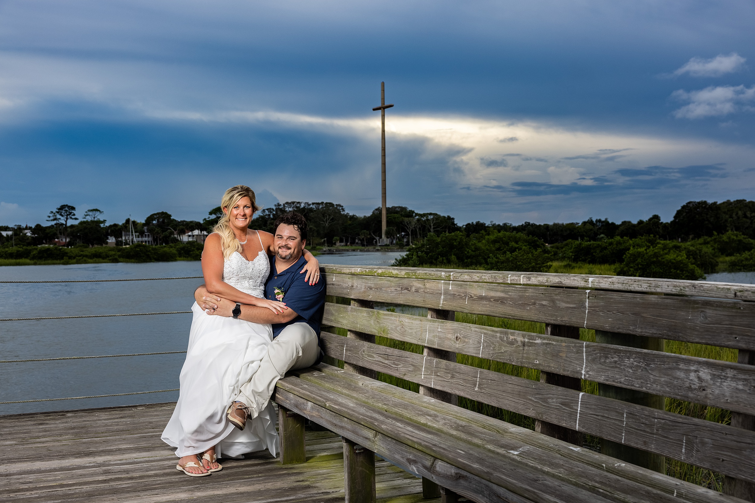 Newlyweds sit on a boardwalk bench at sunset on the river at their fountain of youth wedding