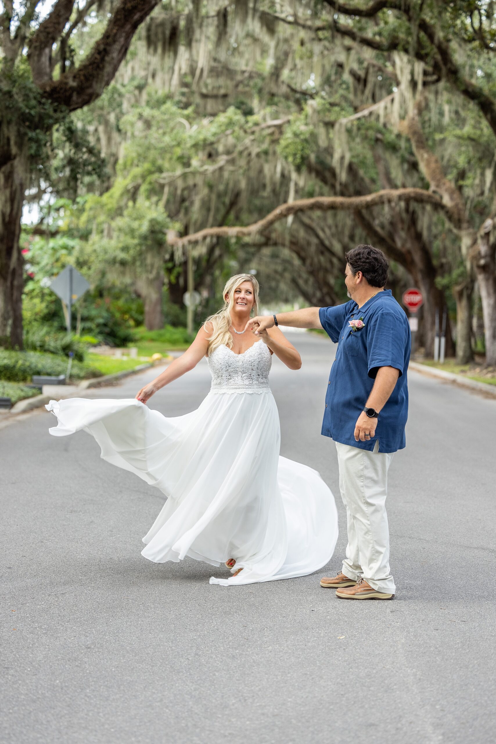 Newlyweds dance and twirl in the street lined with tall oak trees at their fountain of youth wedding