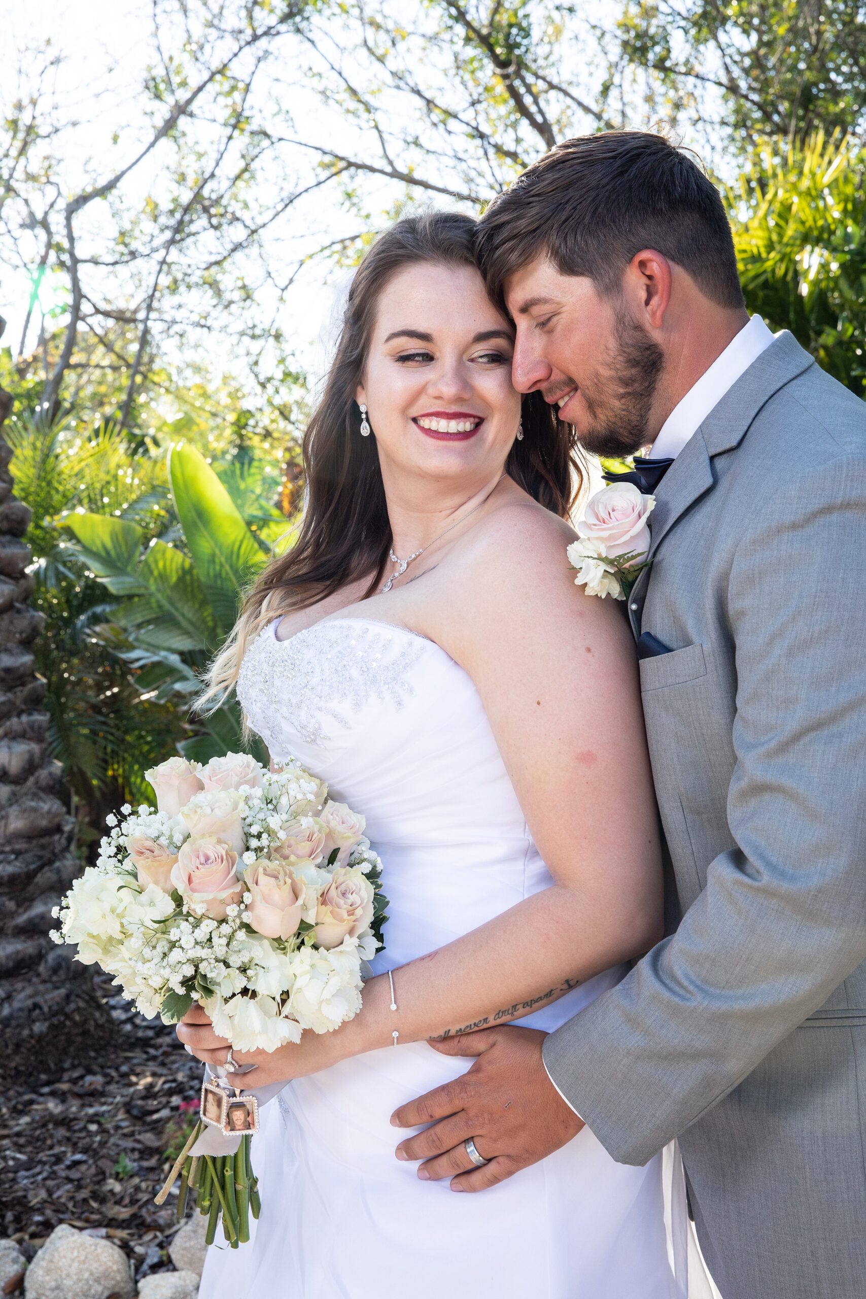Newlyweds smile while standing close in a tropical garden