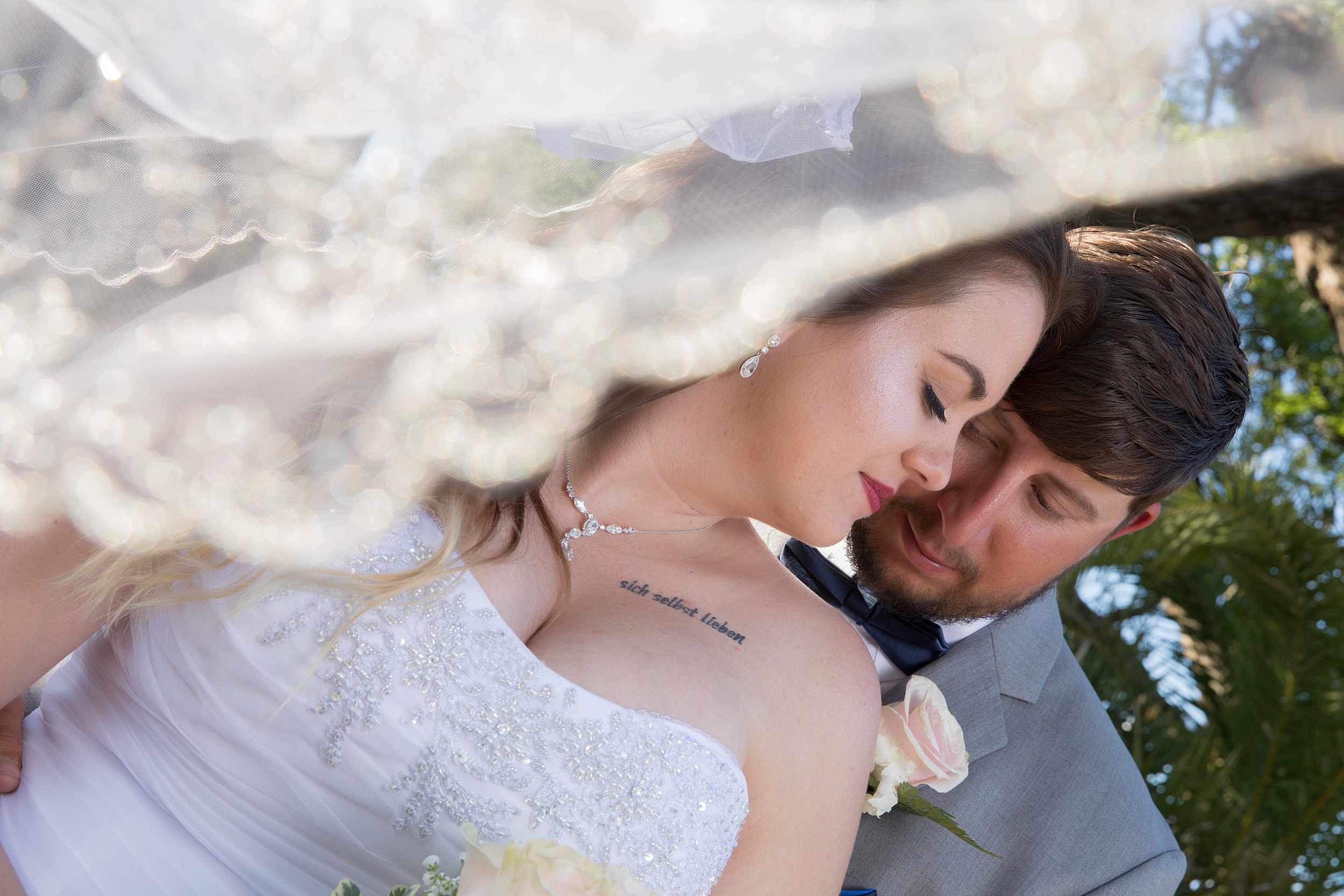 Newlyweds share an intimate moment in a tropical garden while the veil flys around them
