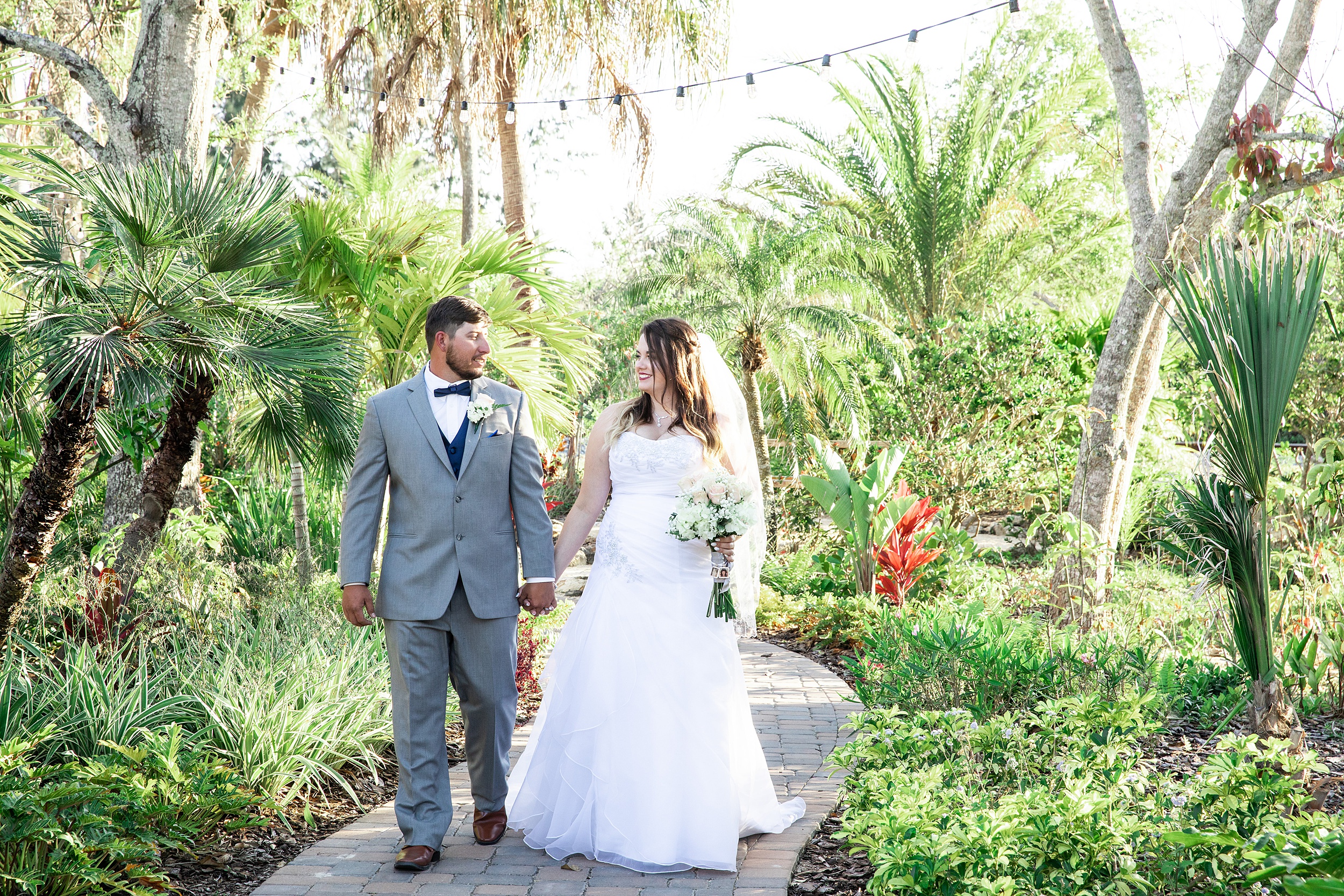 Newlyweds smile while walking through a tropical garden at their historic grant station wedding
