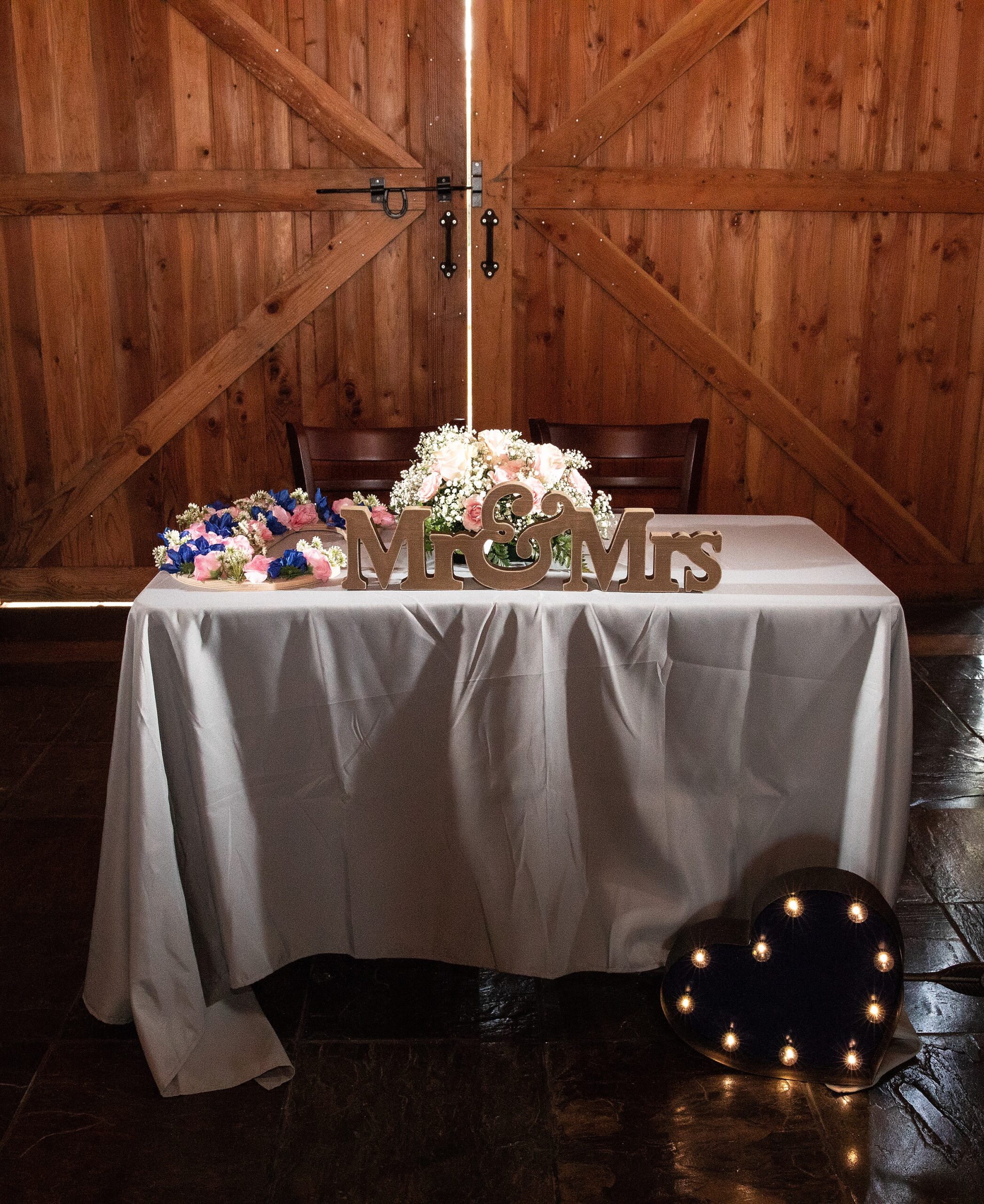 Details of a historic grant station wedding head table with lights and flowers in front of large barn doors