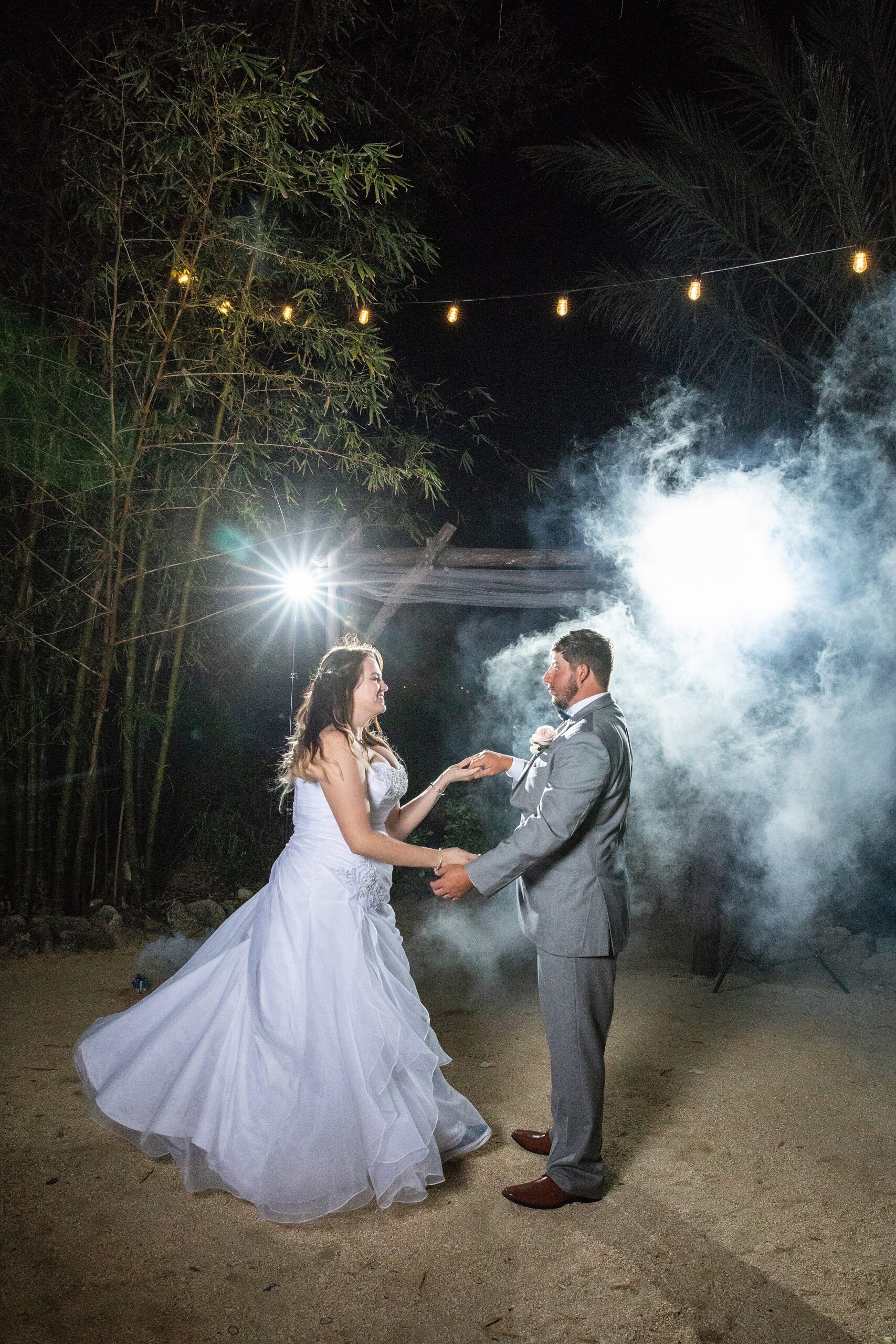 Newlyweds dance in a cloud of smoke outside under market lights at their wedding