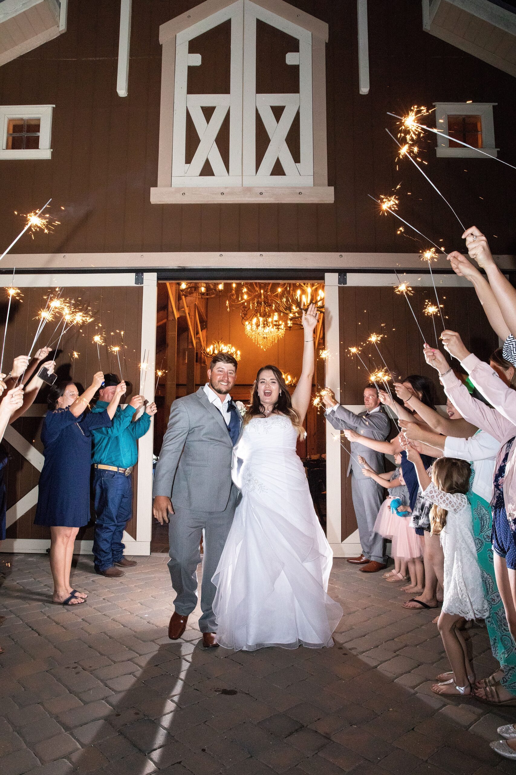 Newlyweds celebrate while exiting a barn to an archway of guests holding sparklers