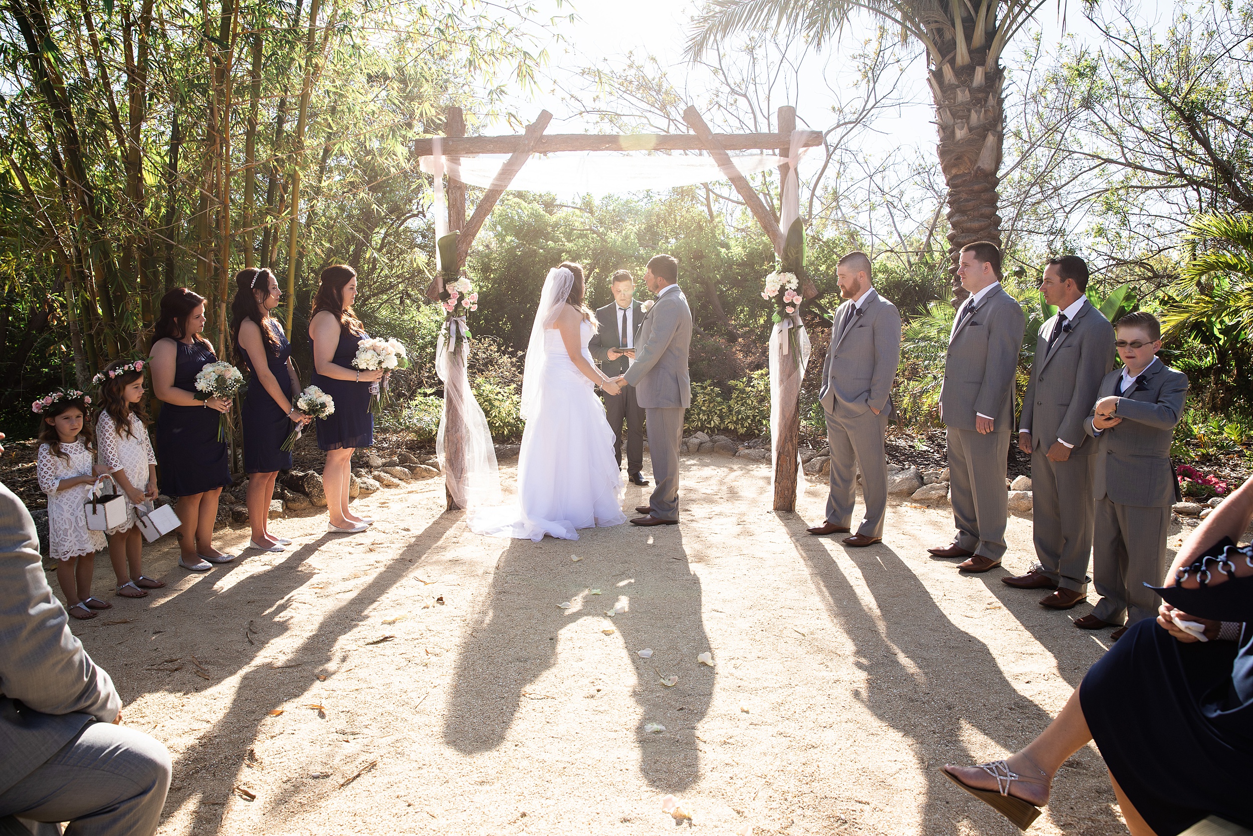 Newlyweds hold hands under a pine beam arbor in a garden at their historic grant station wedding