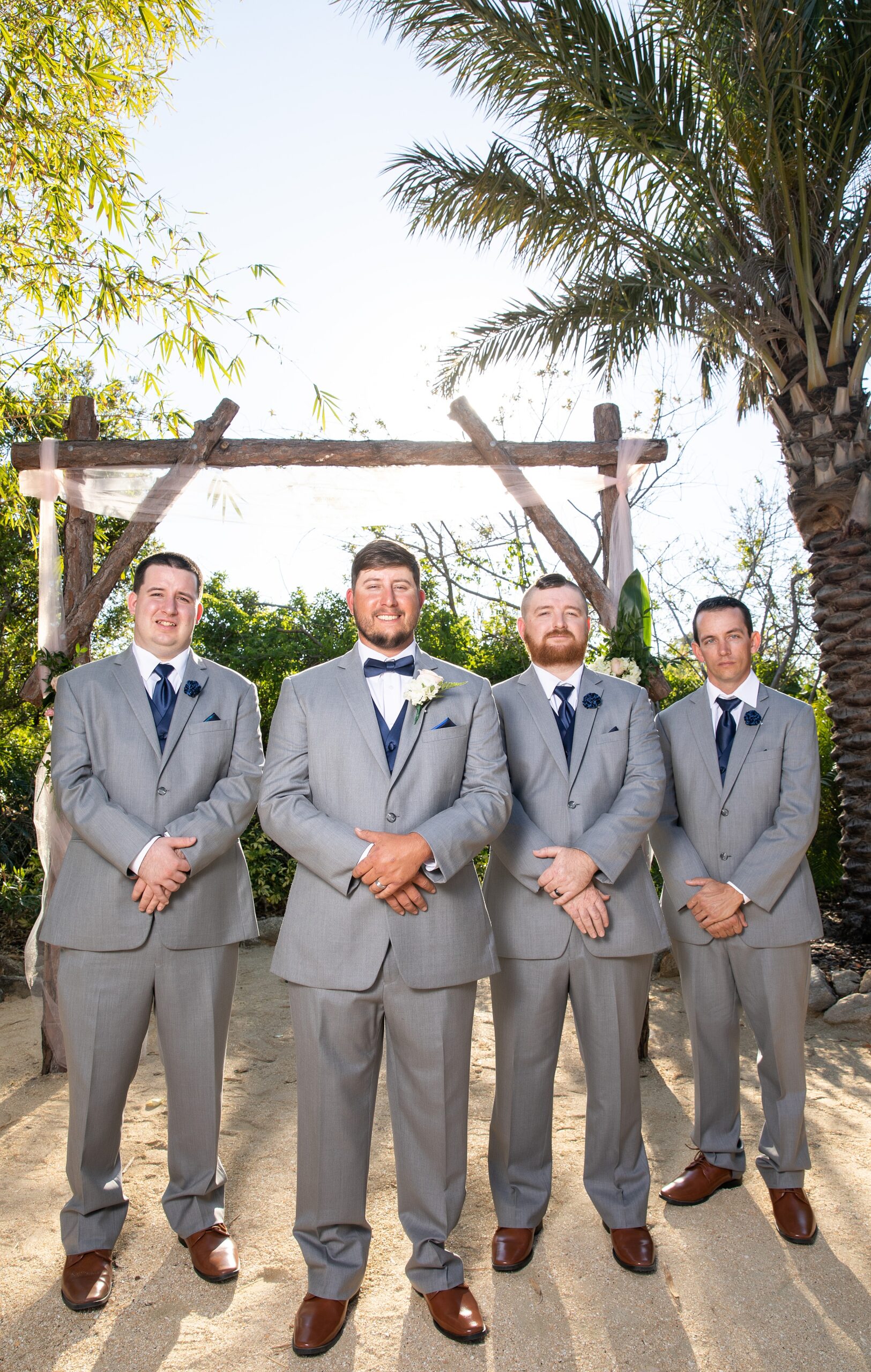 A groom stands with hands crossed in front of him in a grey wuit with his matching groomsmen