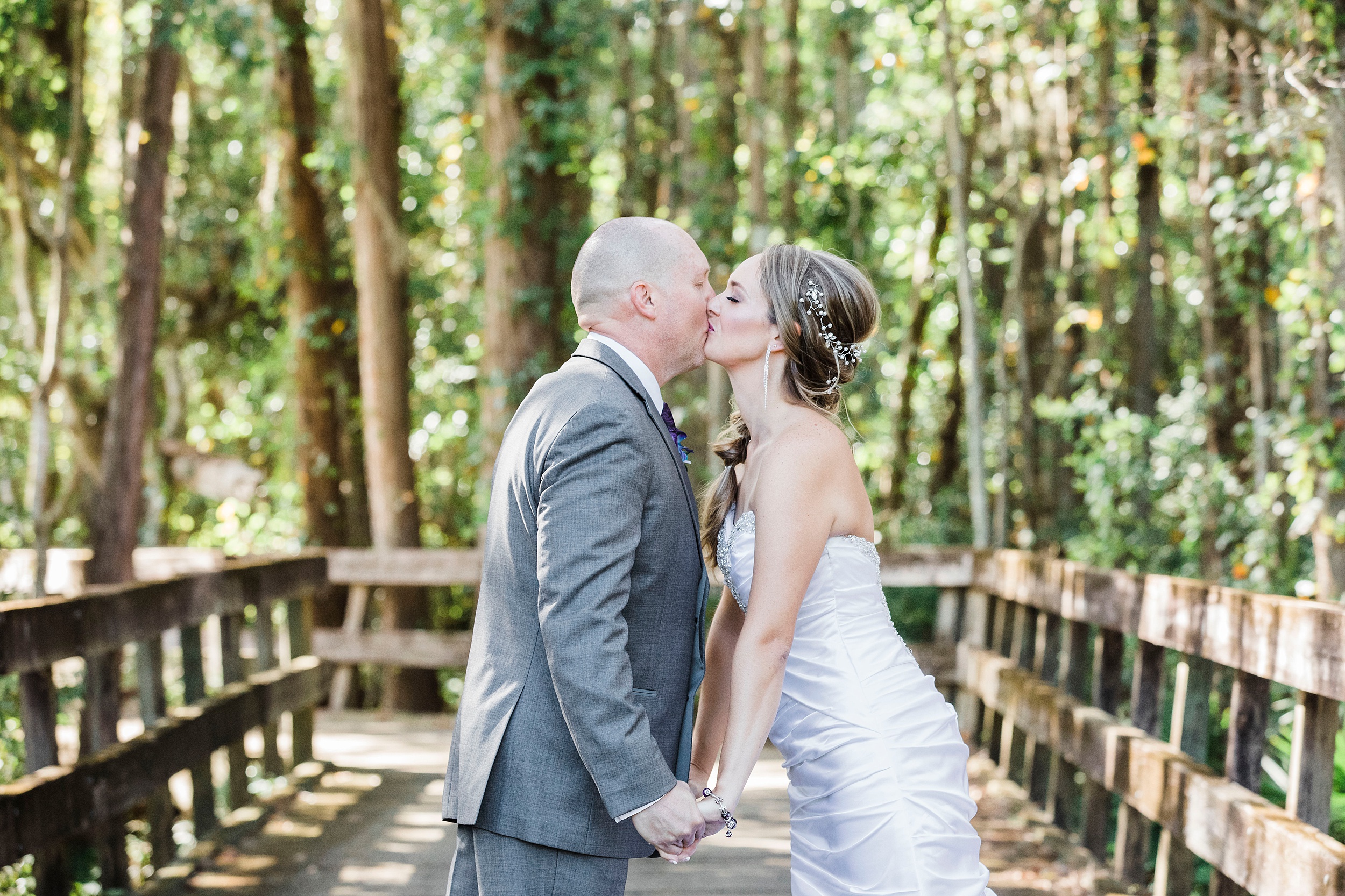Newlyweds kiss on a boardwalk while holding hands at their magnolia point wedding