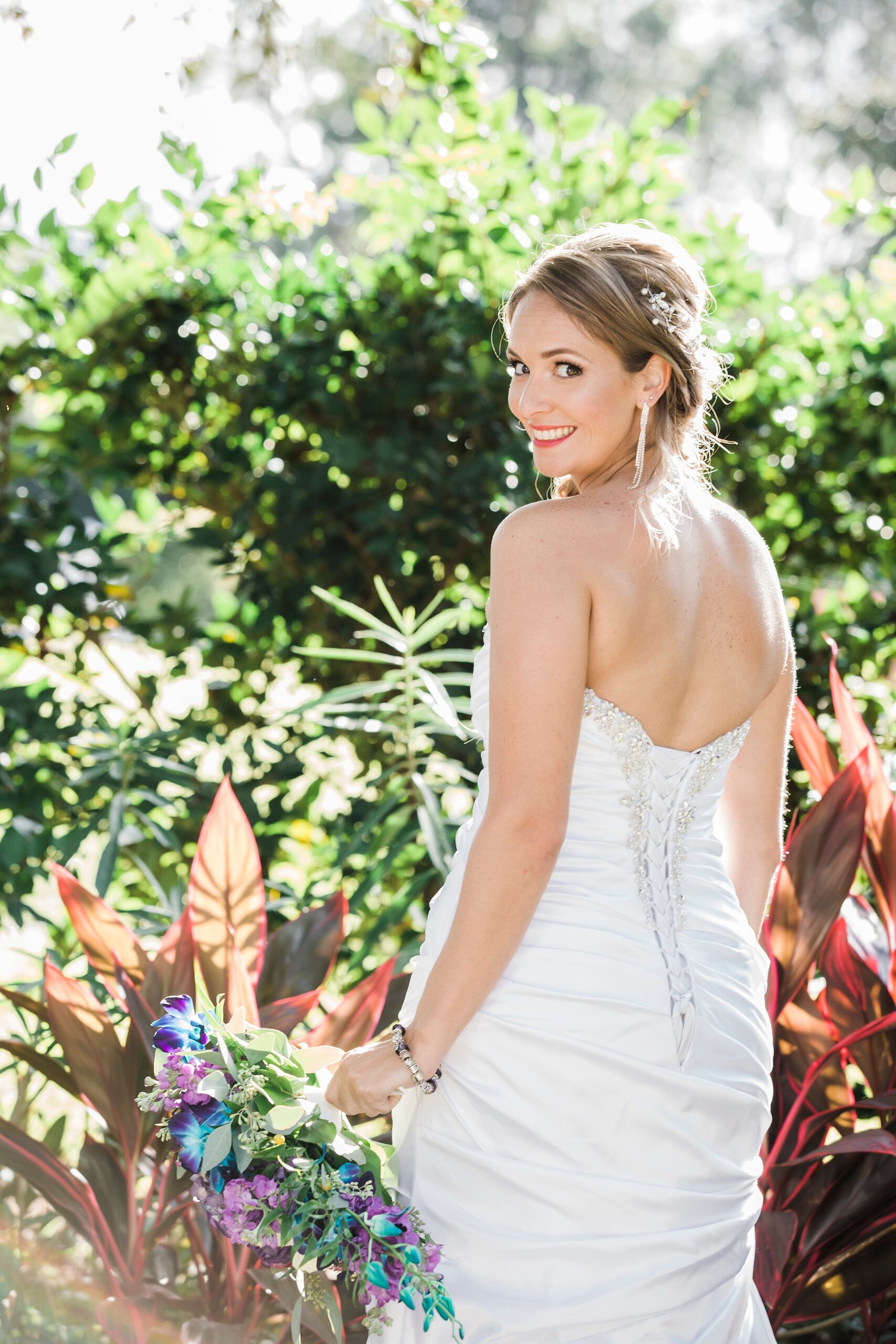 A bride smiles over her shoulder while walking through a garden at her magnolia point wedding