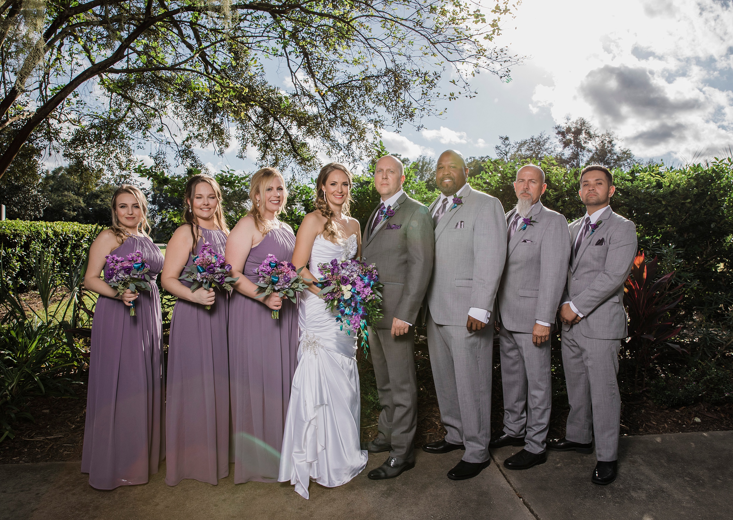 Newlyweds stand in a garden path with their wedding party surrounding them