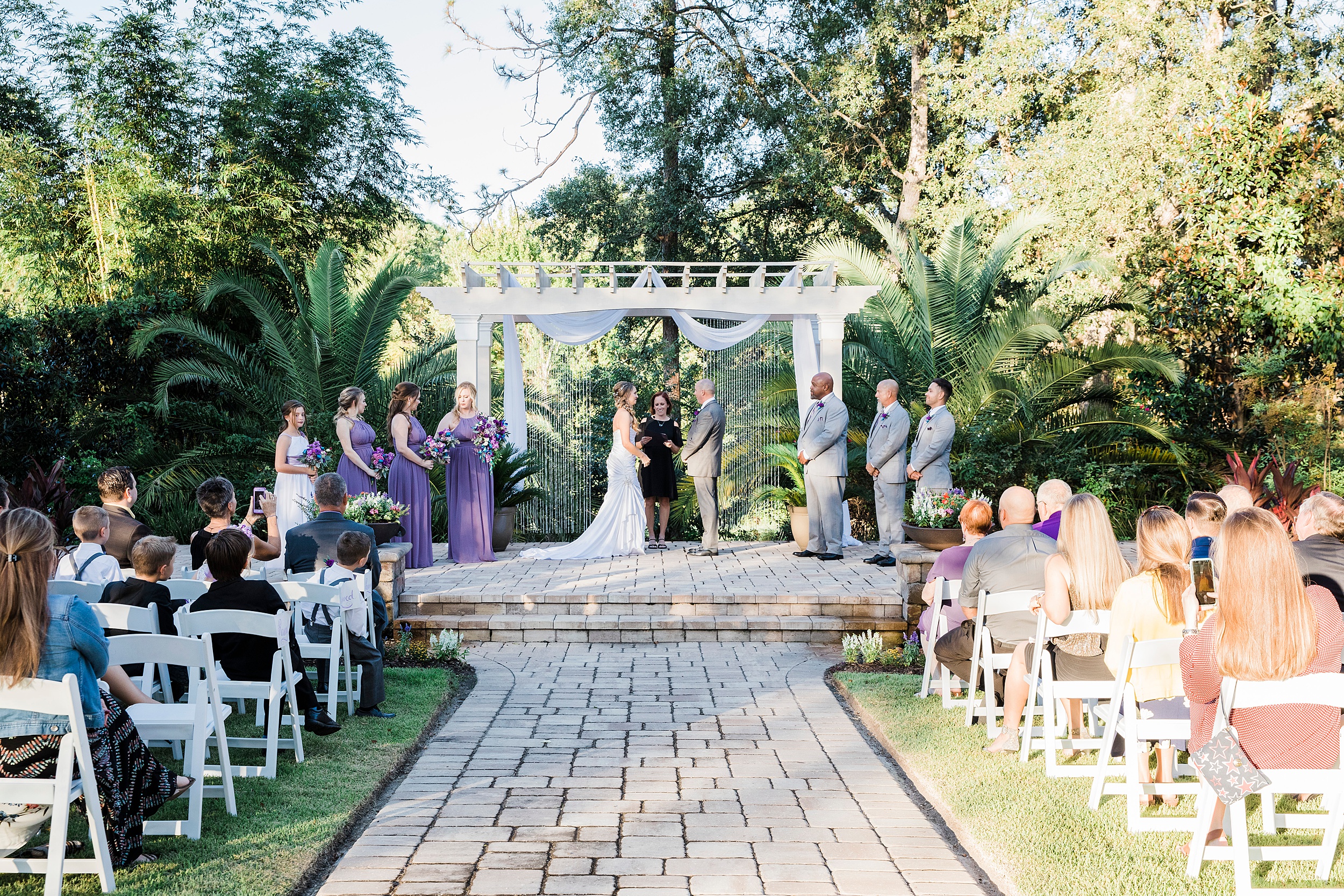 A bride and Groom stand under a white pergola facing each other during their magnolia point wedding ceremony