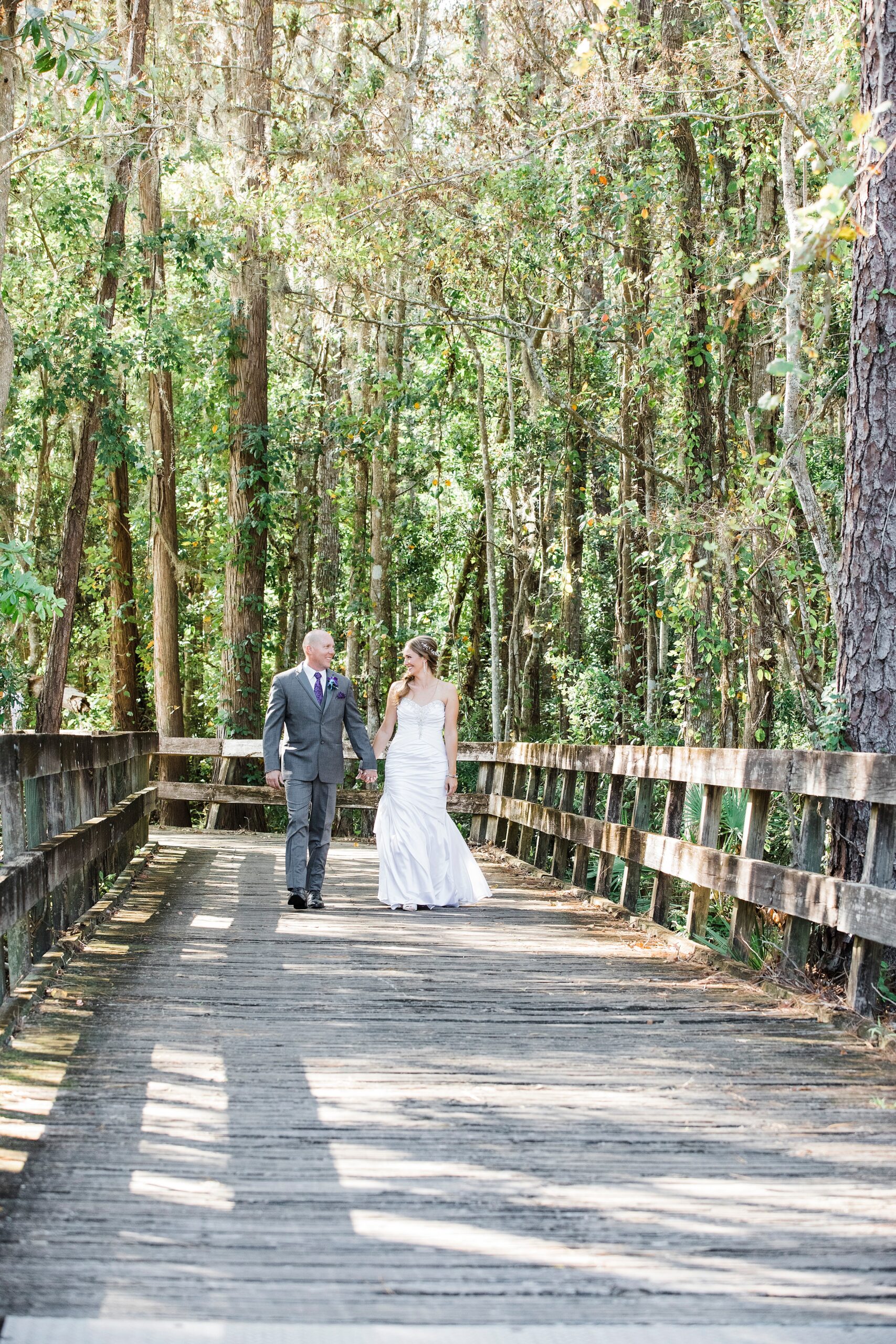 Newlyweds hold hands while walking up a wooden boardwalk at their magnolia point wedding