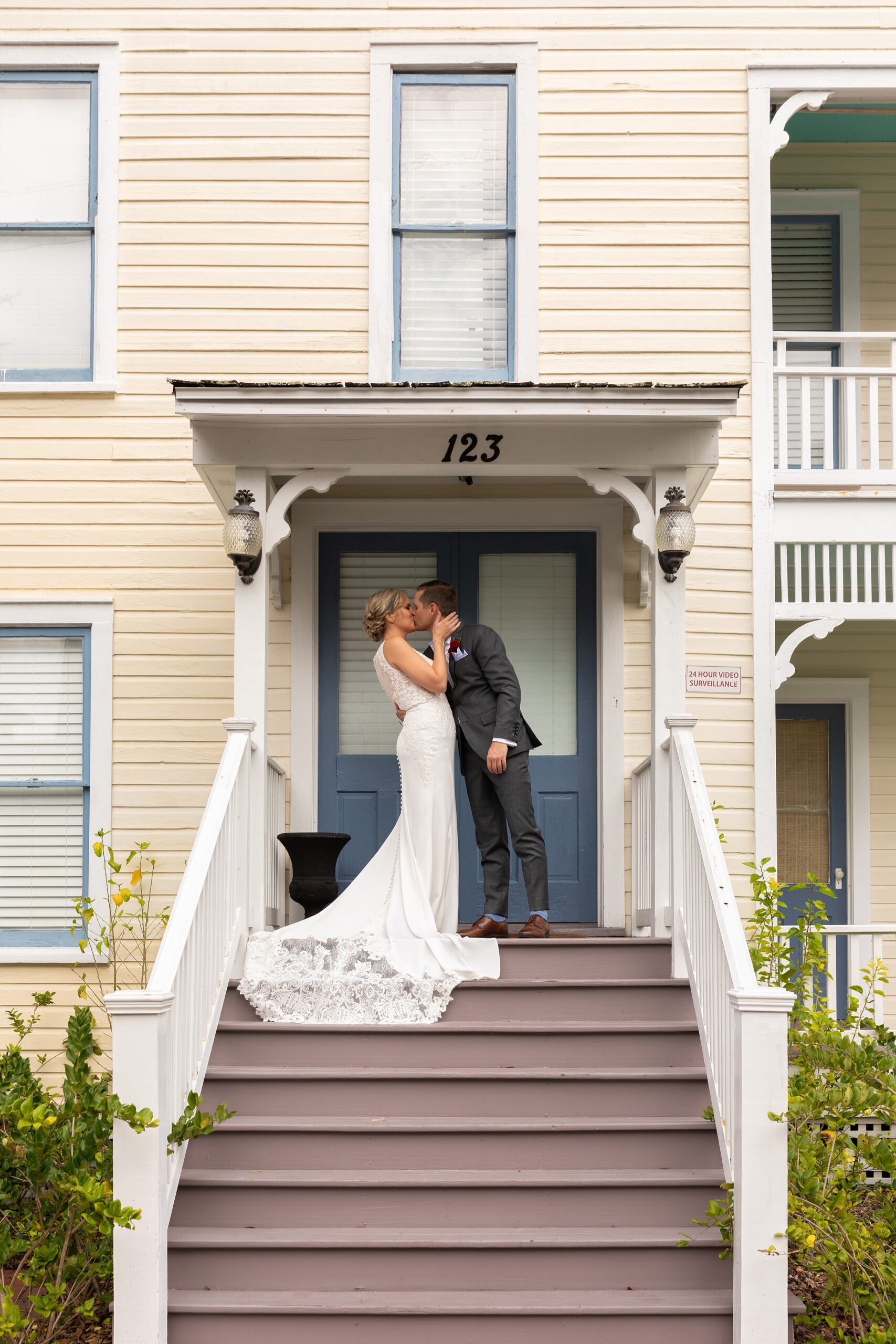 Newlyweds kiss on a front porch of a cream building