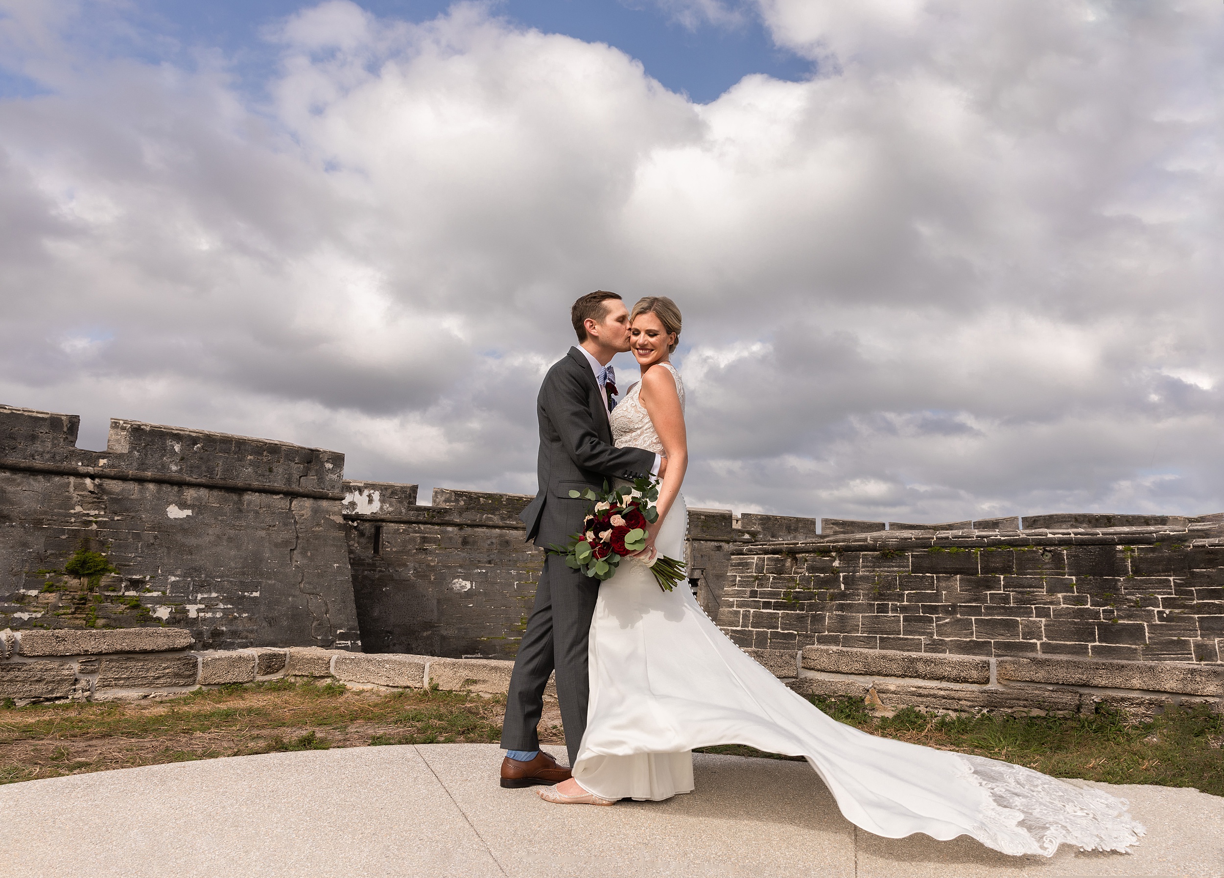 Newlyweds kiss and stand on a patio by historical walls