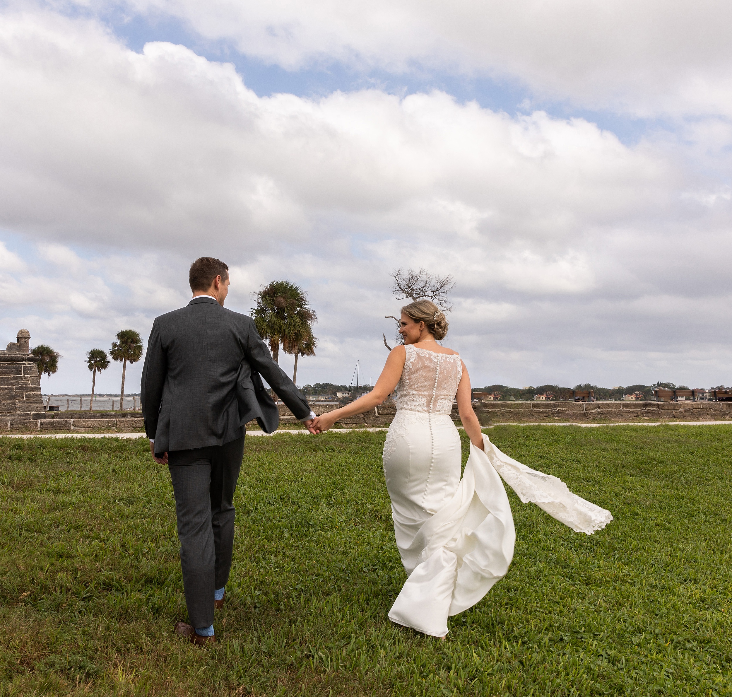 Newlyweds hold hands while walking through a grassy lawn
