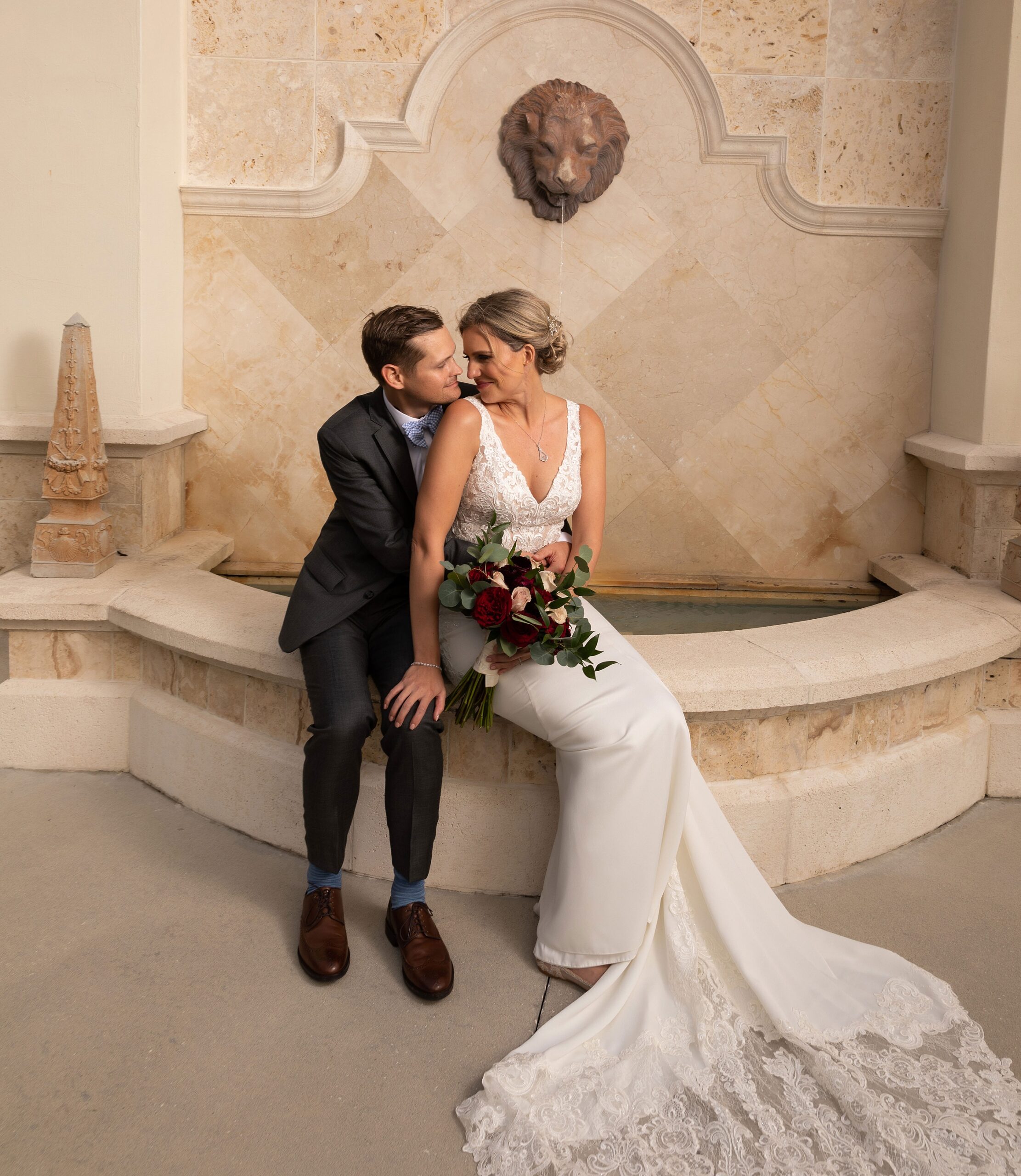Newlyweds sit on the edge of a marble indoor fountain