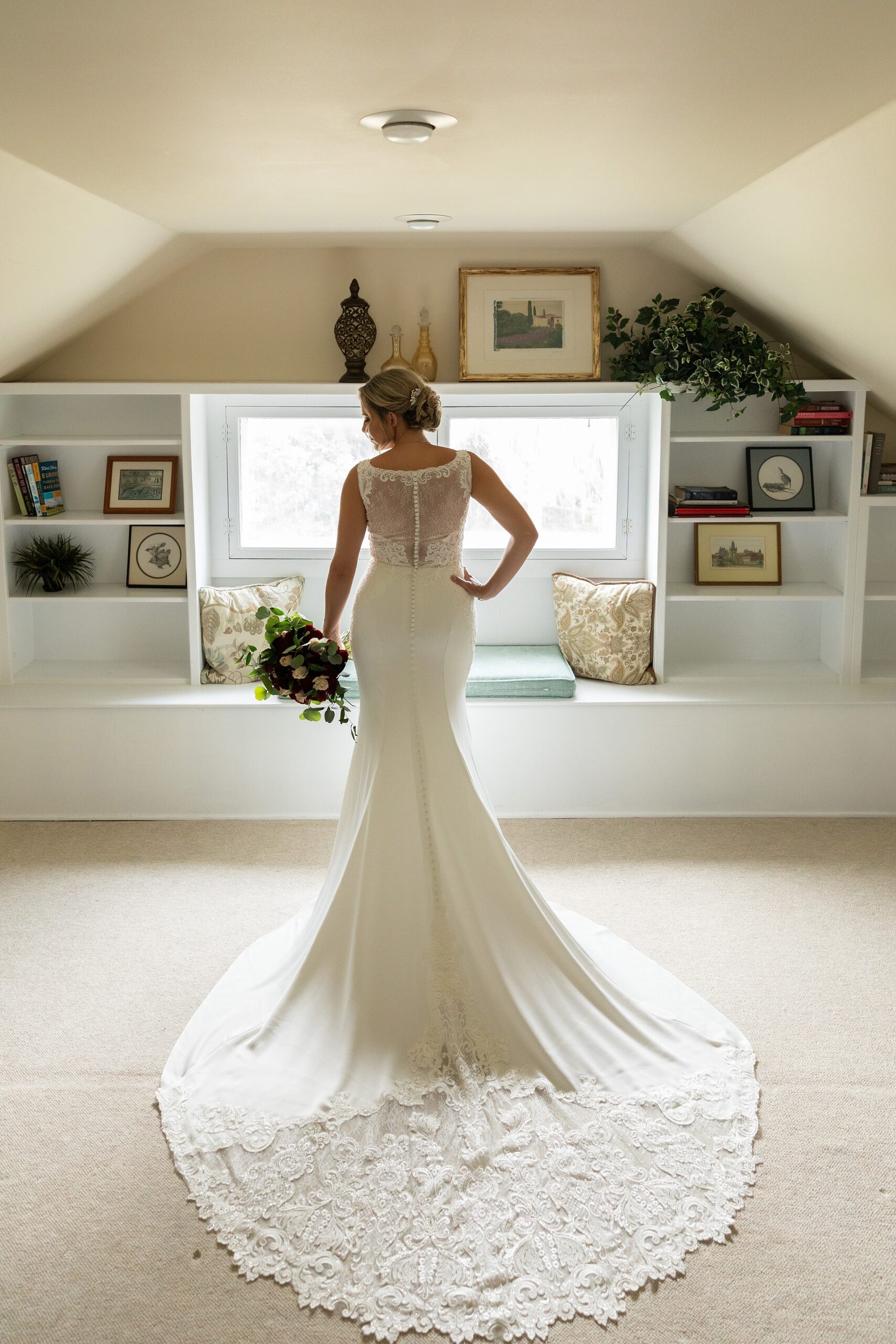 A bride stands in a window showing off her long train and bouquet