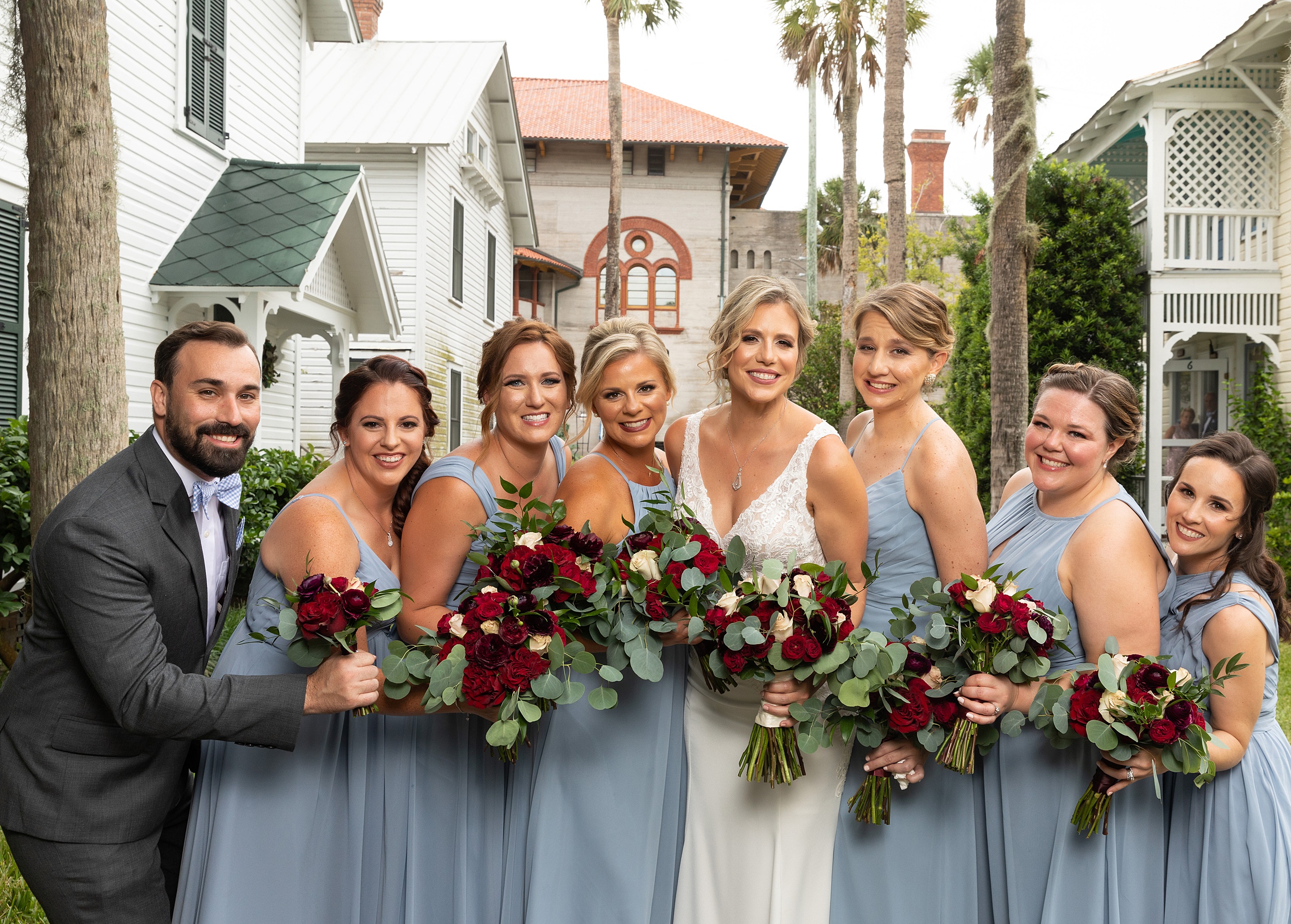 A bride stands outside holding her bouquet with her bridesmaids in blue dresses
